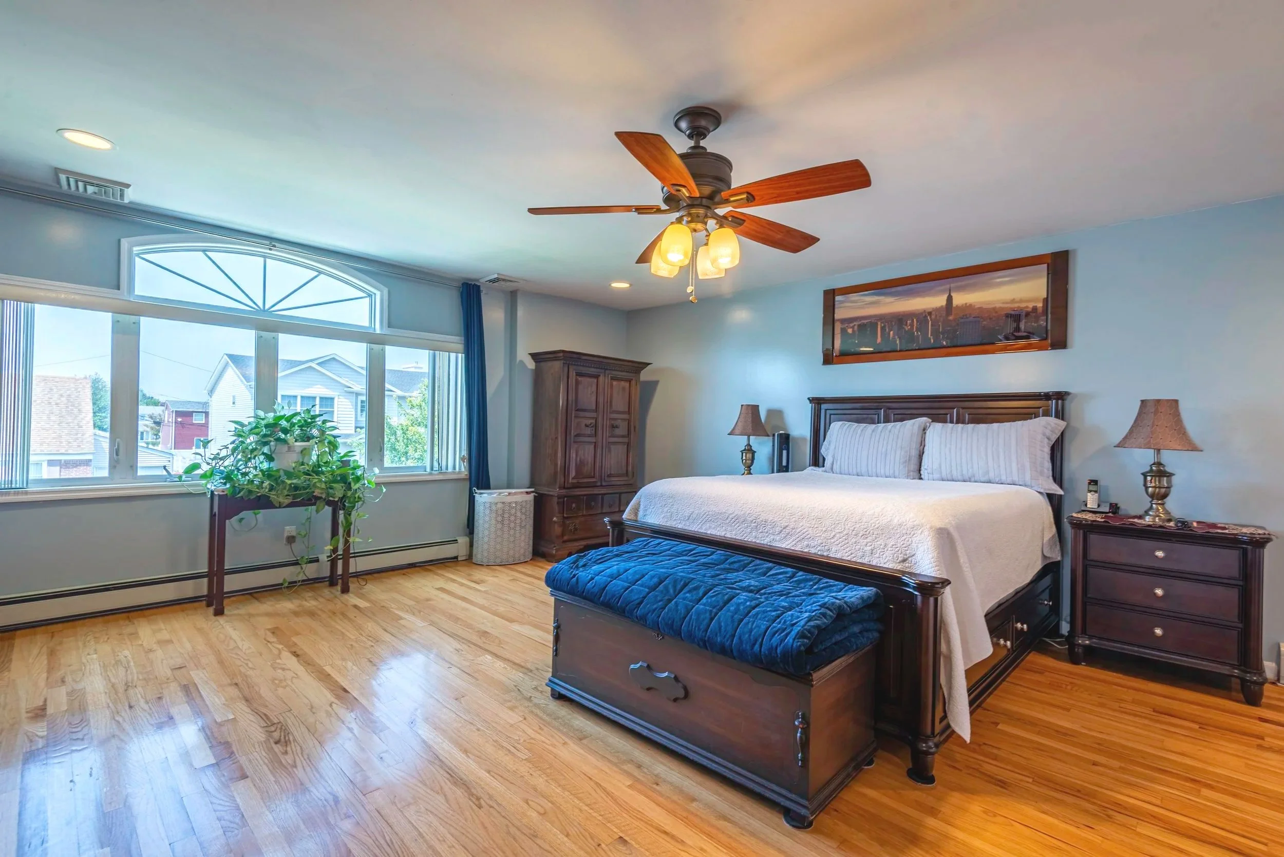 Stylish bedroom featuring blue walls, hardwood flooring, ceiling fan, and large window with natural light.