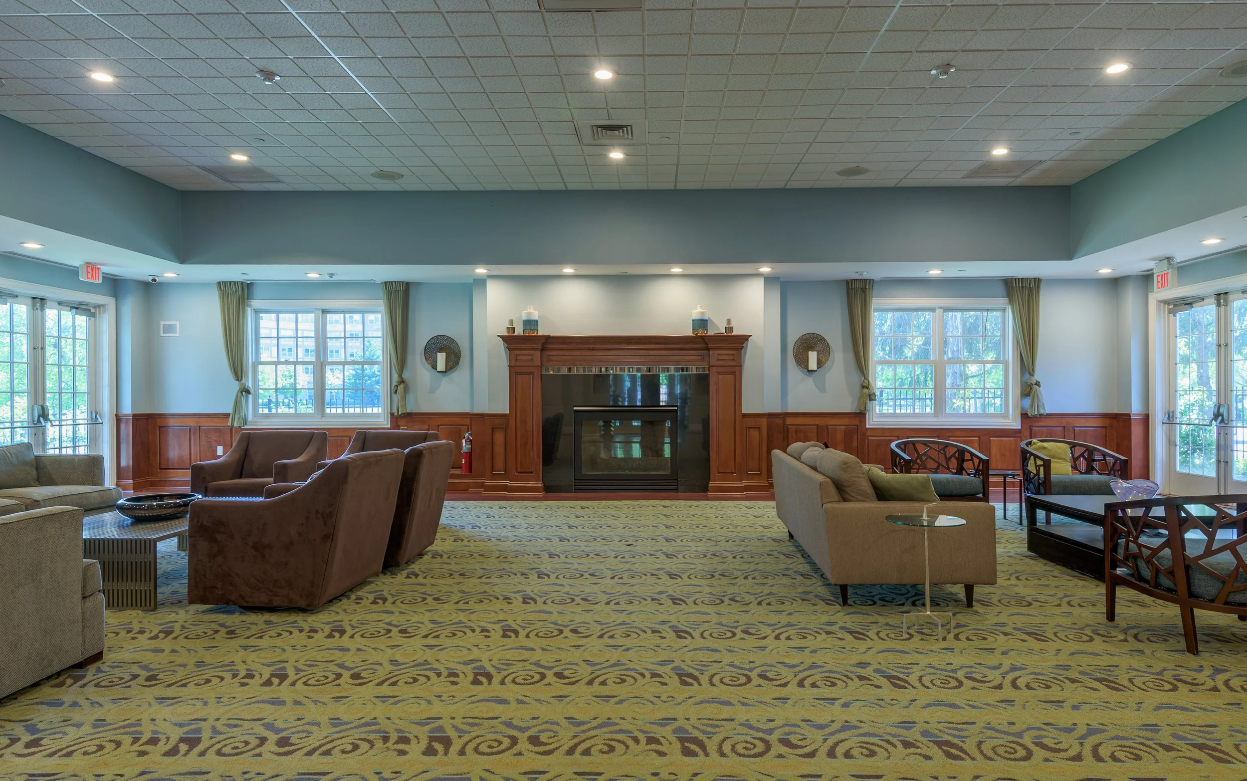 Interior lounge at The Addison senior living community featuring seating areas, fireplace, and large windows