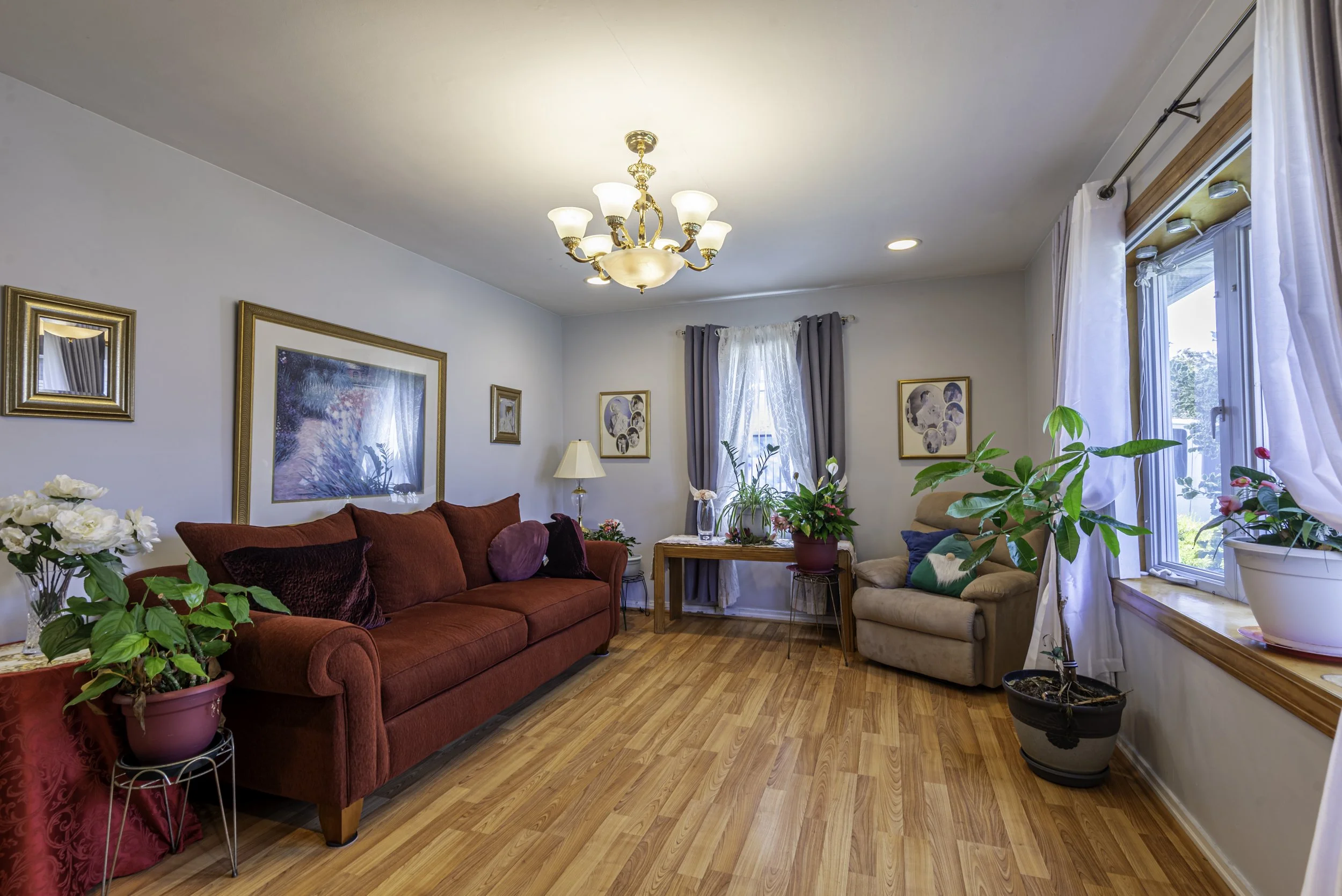 Cozy living room with hardwood floors, elegant chandelier, red sofa, neutral walls, and large window bringing in natural light.