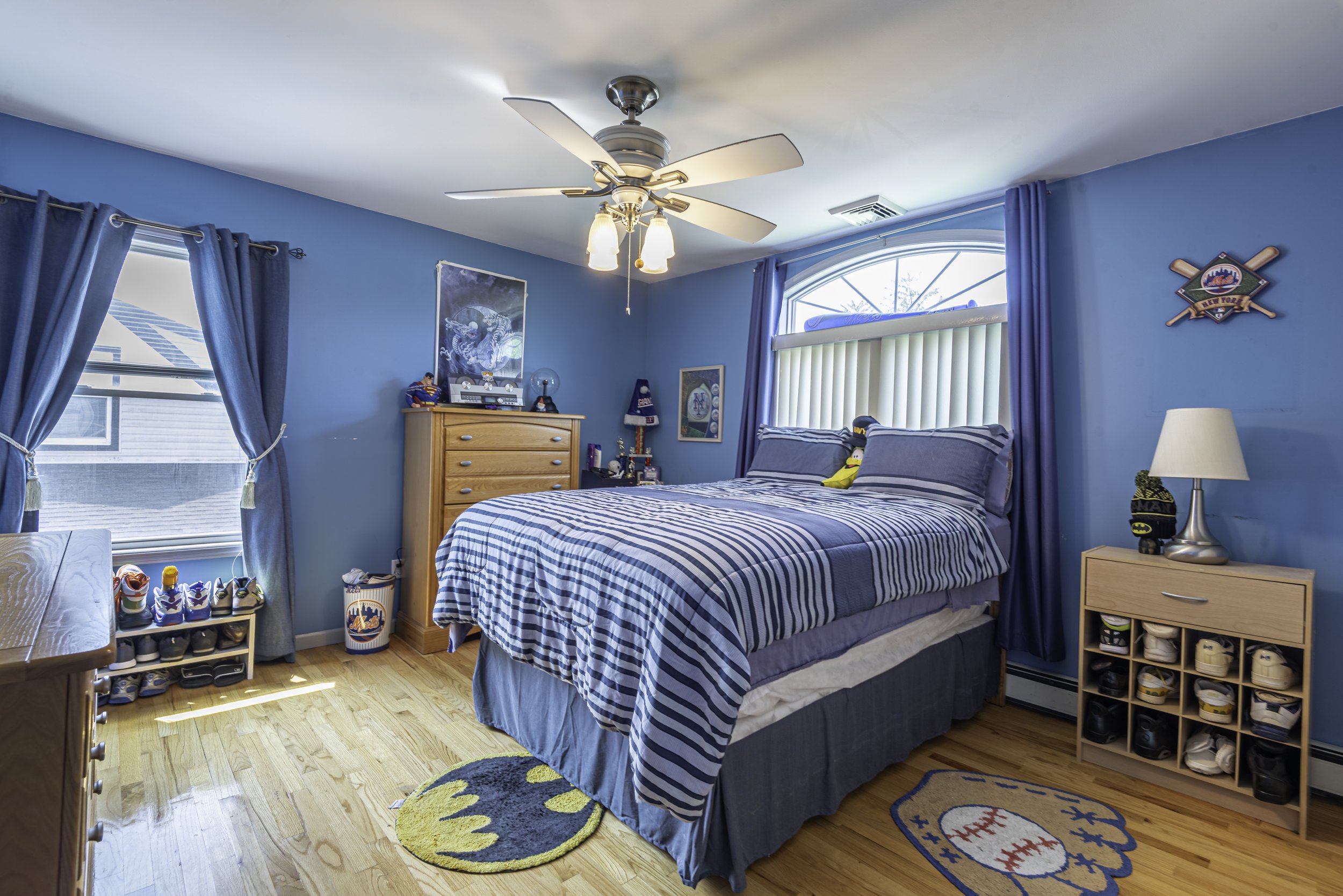 Large master bedroom with hardwood flooring, ceiling fan, stylish dark wood furniture, and bright window views.