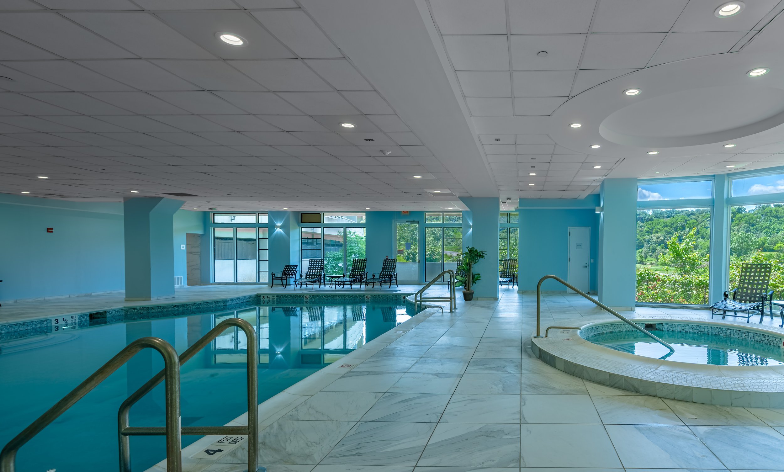 Indoor pool and spa at The Addison senior living community with large windows and lounge seating
