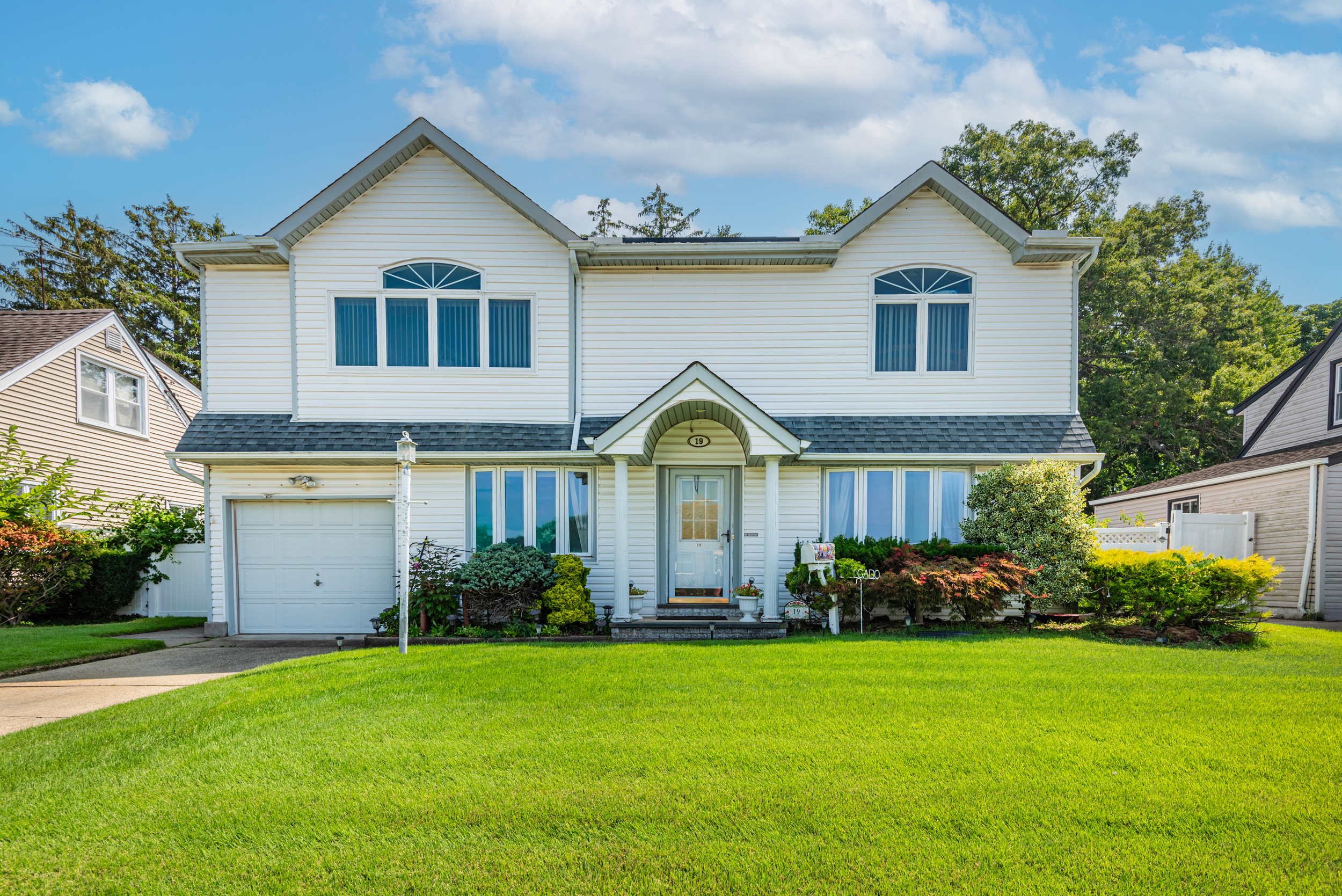 Real estate photo of a white colonial-style house with green lawn, symmetrically placed windows, and manicured landscaping.