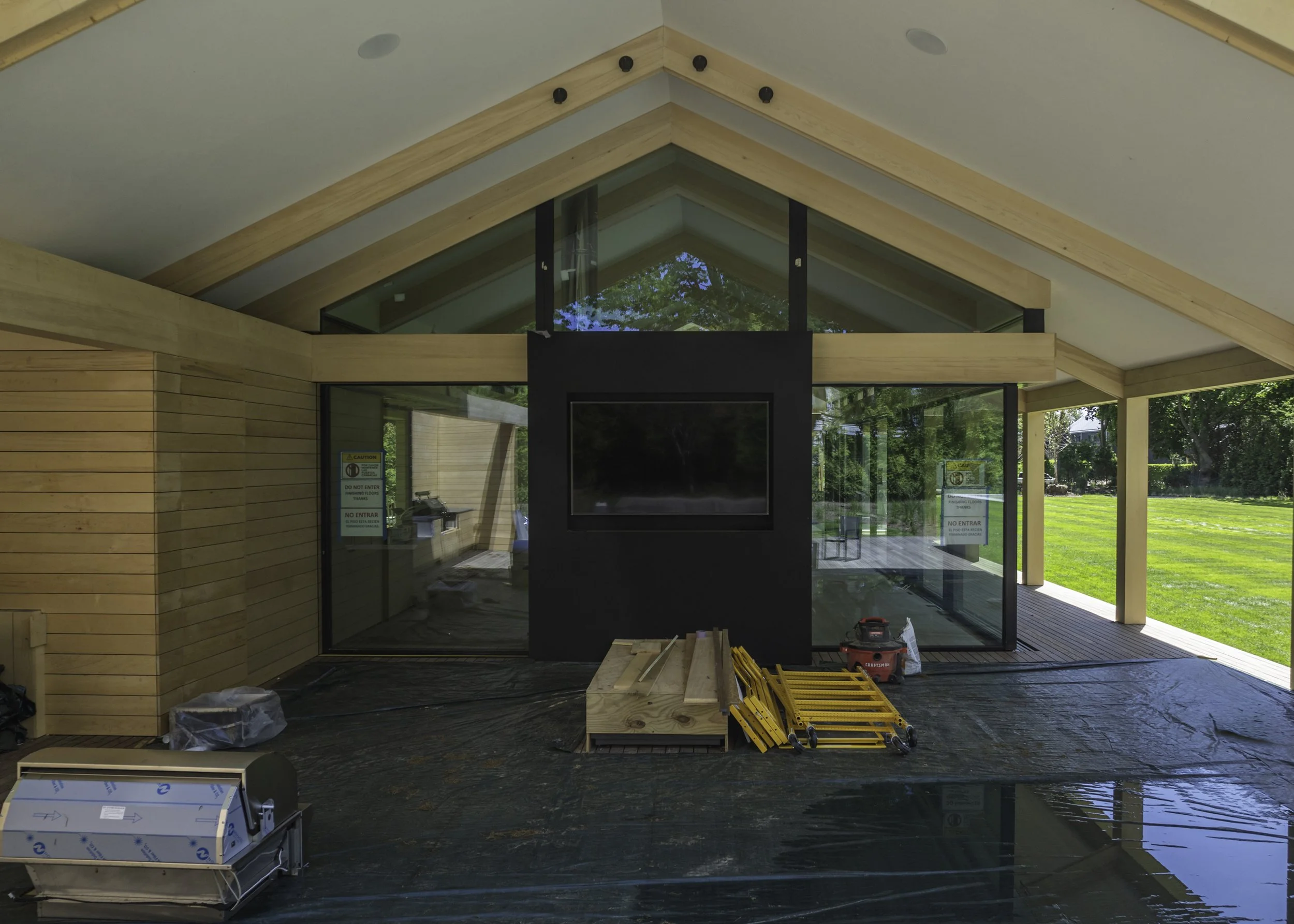 Covered outdoor patio under construction with exposed materials, fireplace, and protective floor covering.