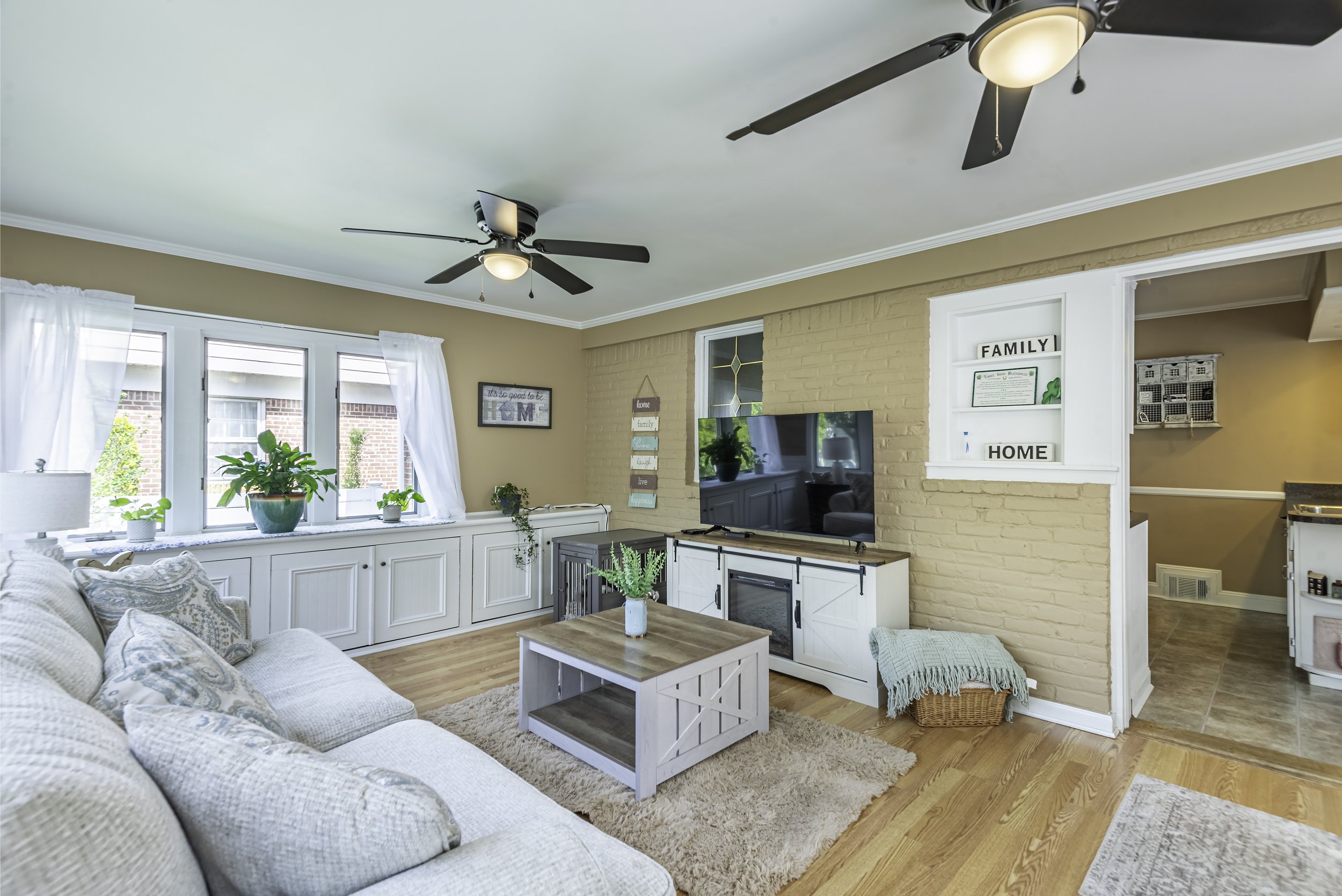 Welcoming family room with multiple windows, farmhouse decor, comfortable sofas, ceiling fan, and stylish built-in cabinets.