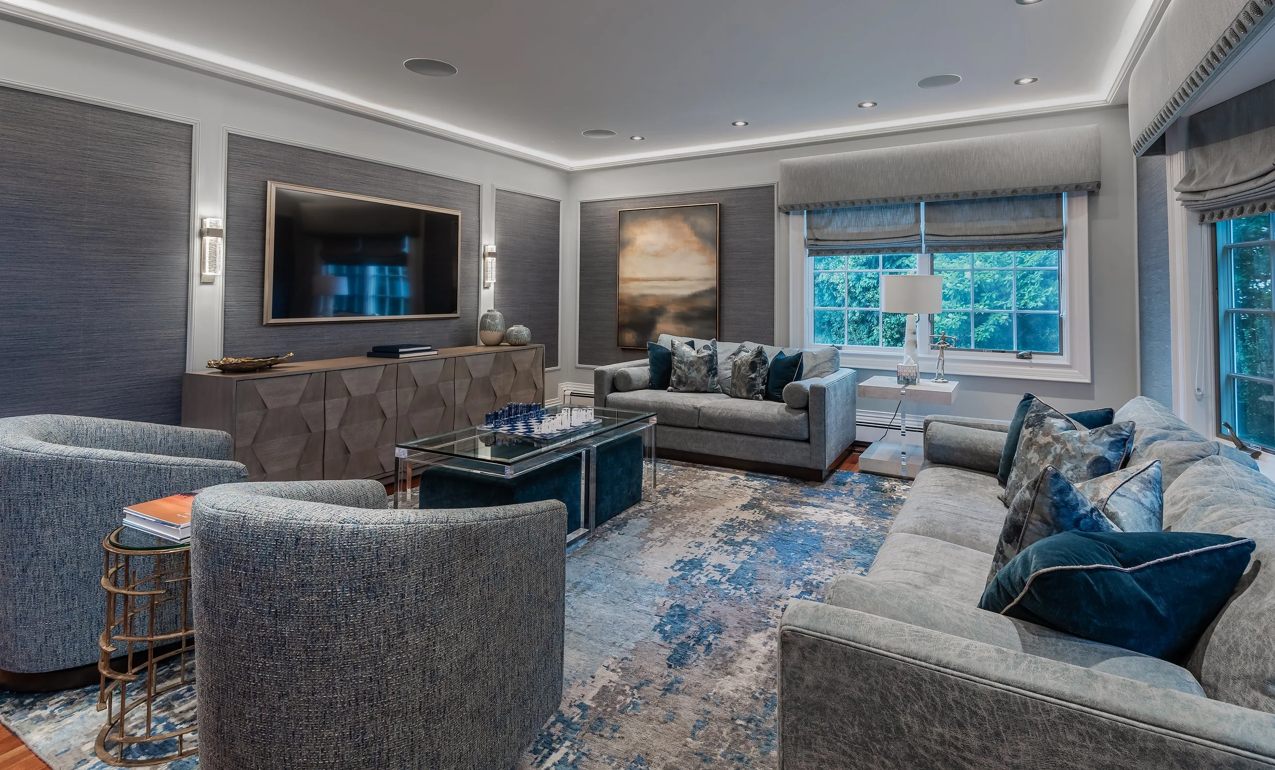 Modern blue and gray living room with contemporary furniture, recessed ceiling lighting, and large window bringing in natural light.