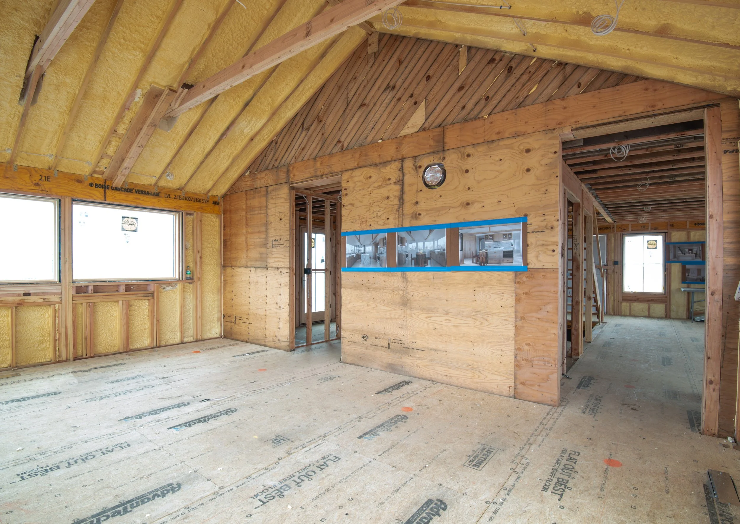 Kitchen of a Hamptons home during a full gut renovation, with exposed rafters, spray foam insulation and kitchen design renderings taped to the framing