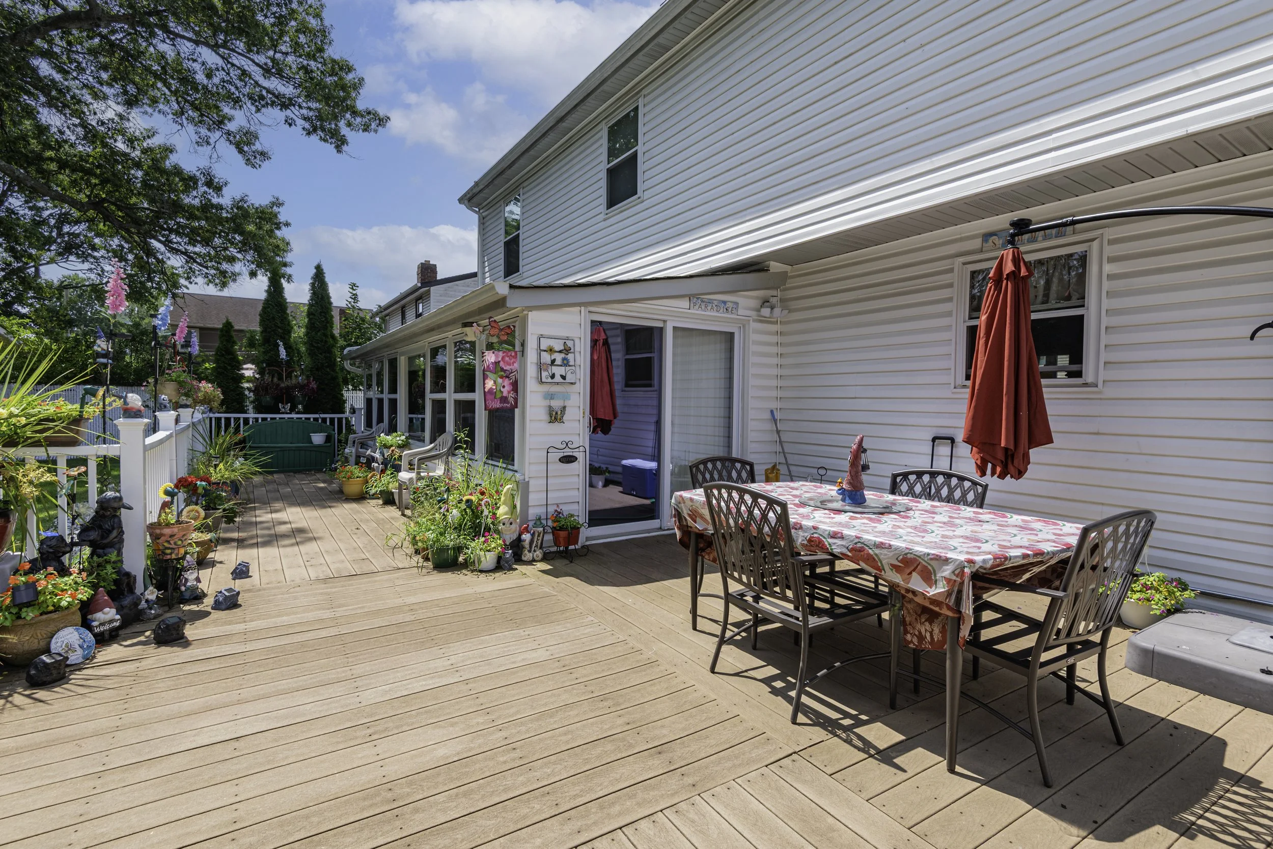 Sunny backyard patio with outdoor dining table, grill, landscaped plants, and fenced yard—perfect for entertaining.