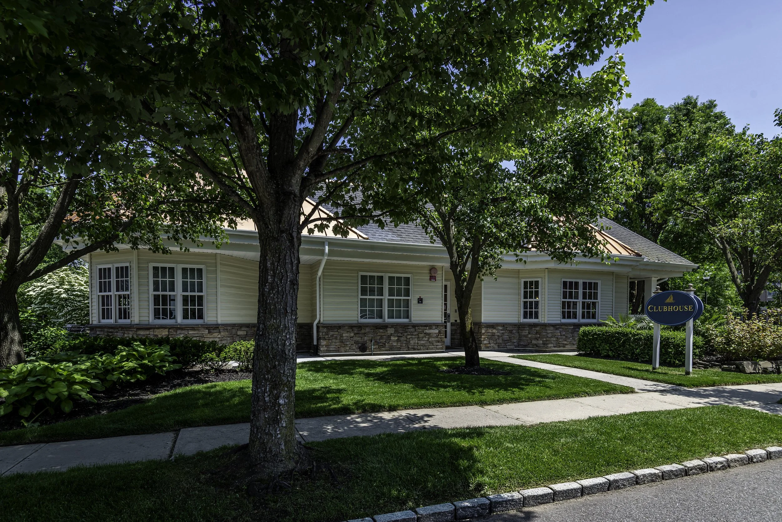 Wide exterior view of The Addison senior living community clubhouse surrounded by trees and green landscaping.