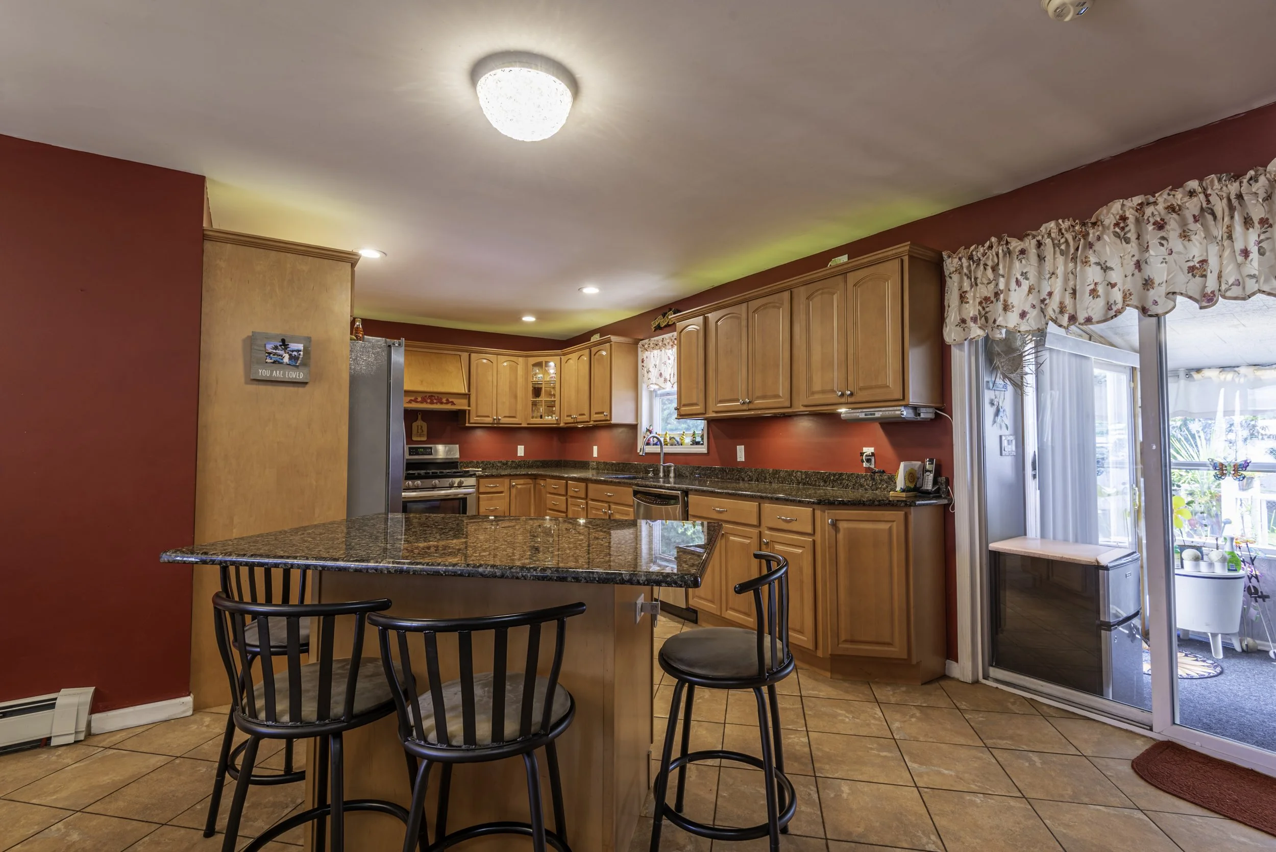 Spacious kitchen with granite countertops, wood cabinetry, tile flooring, stainless steel appliances, and a center island with seating.