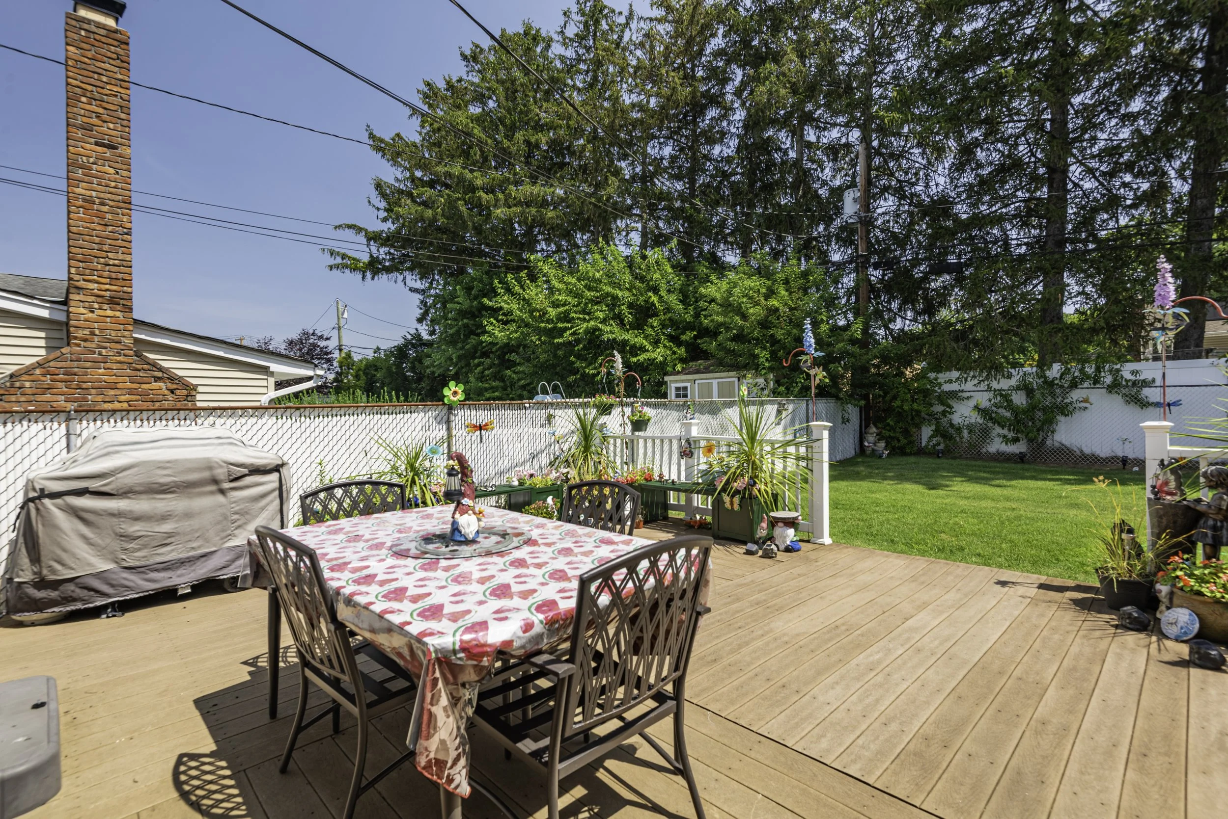 Spacious backyard deck with multiple seating areas, patio table, landscaping, and access to the home’s sunroom.
