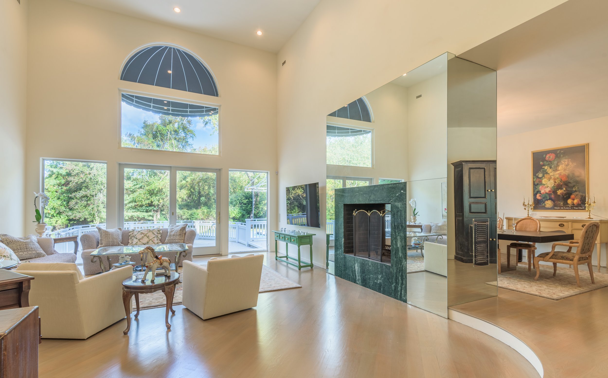 Bright luxury living room interior with high ceilings, large windows, elegant décor, mirrored fireplace, and natural light — captured for real estate and architectural photography.