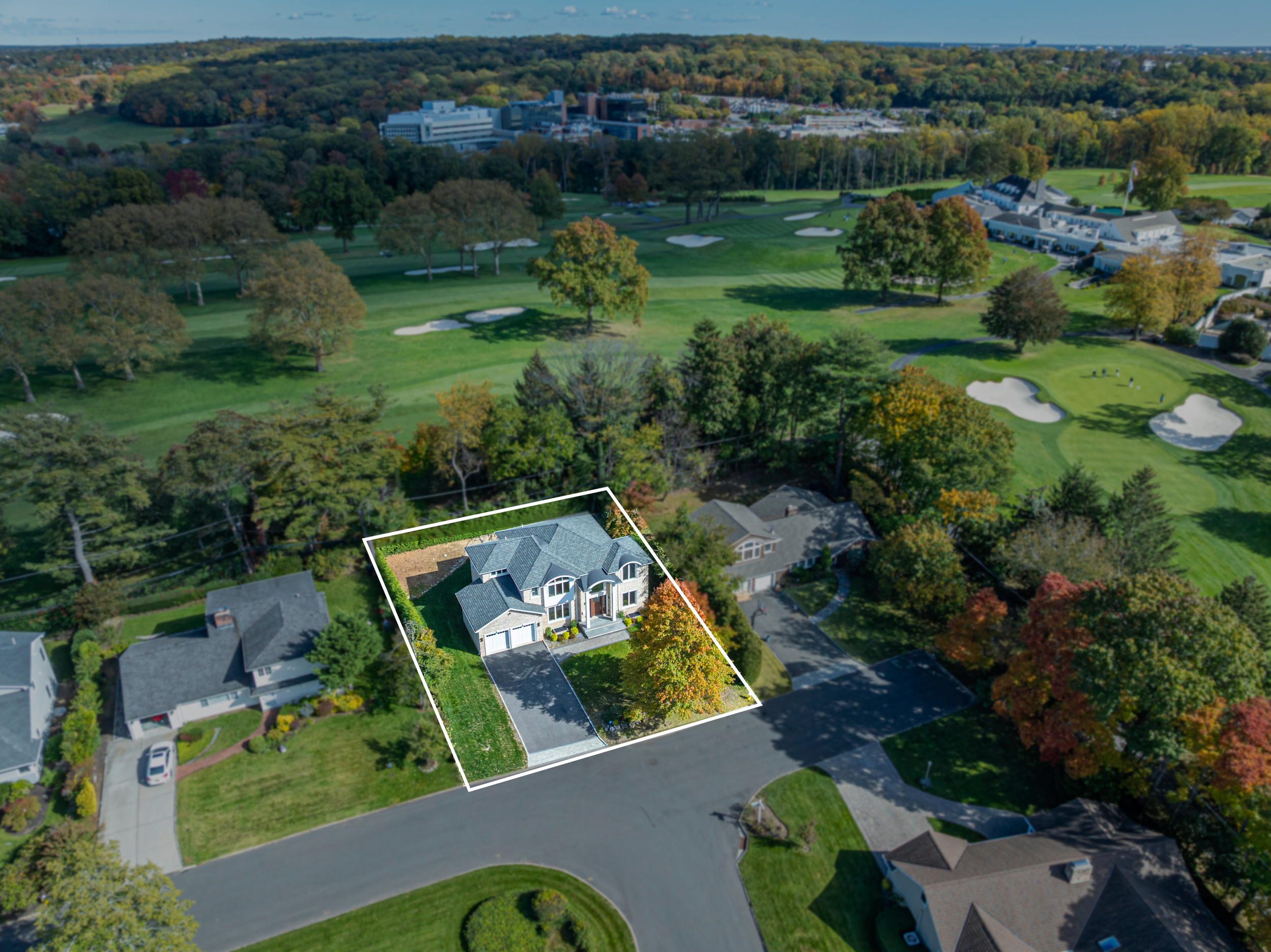 Professional drone photograph showing a highlighted property lot surrounded by mature trees, neighboring homes, and a nearby golf course.