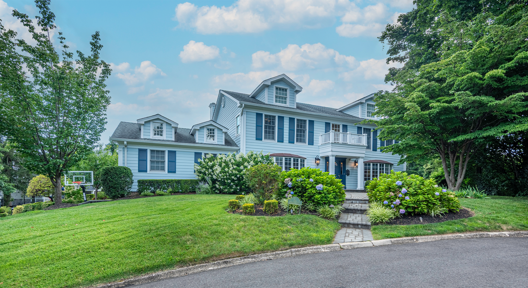 Front exterior of colonial-style house with blue shutters and well-maintained landscaping.
