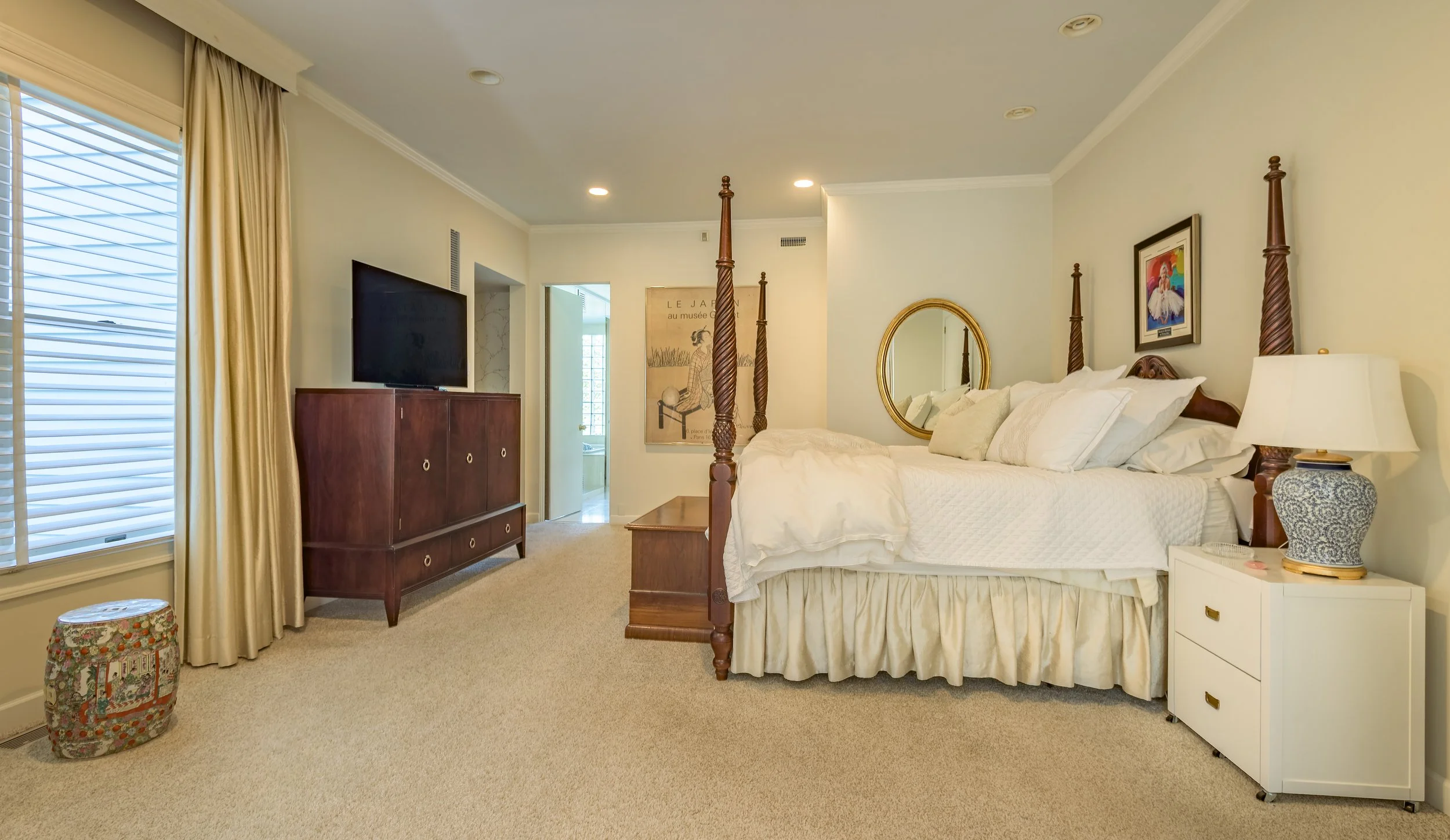 Elegant master bedroom interior with four-poster bed, soft lighting, neutral decor, modern furnishings, and attached bathroom — photographed for real estate and architectural marketing.
