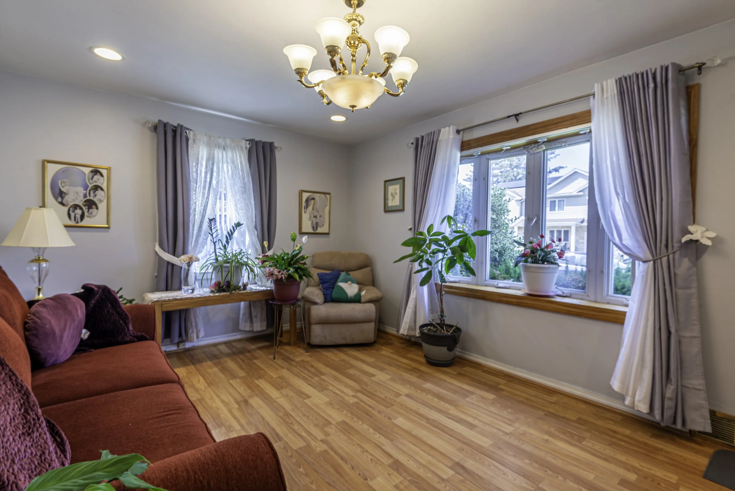 Bright entryway and living room with hardwood flooring, staircase, decorative console table, and large window with curtains.