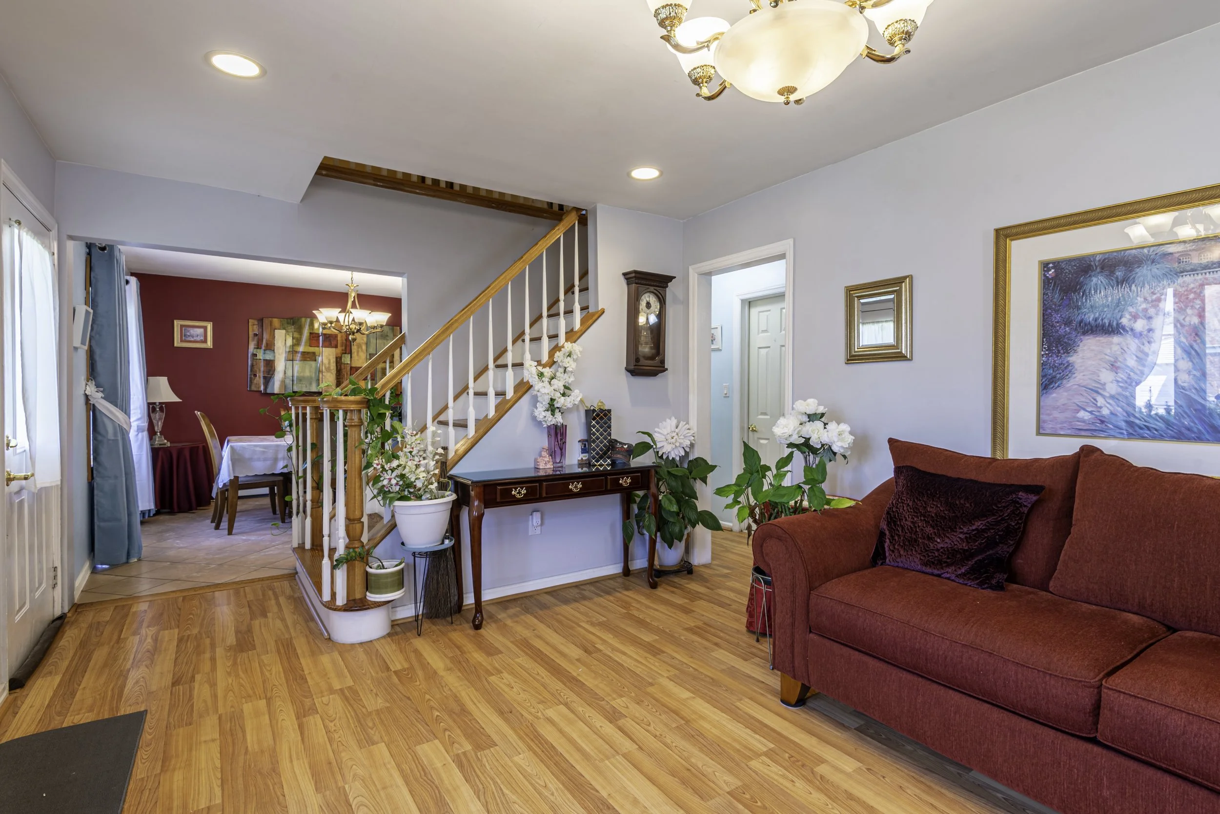 Inviting living room featuring hardwood floors, large front window, comfortable seating, houseplants, and bright natural lighting.