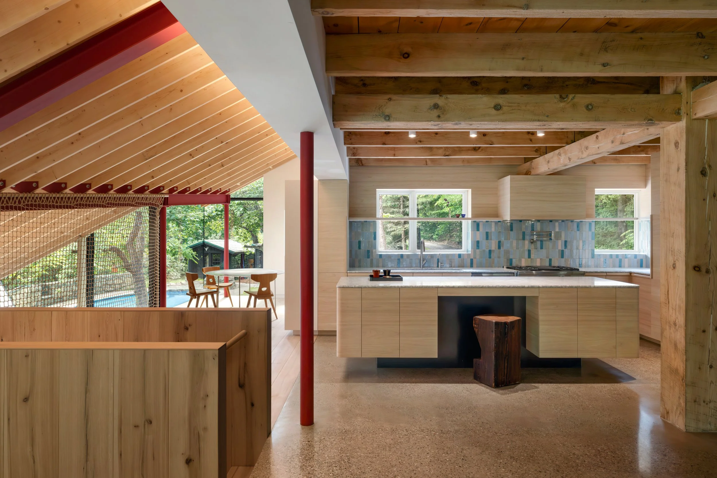 Interior of a modern home with wood accents, a kitchen with a countertop, and a seating area with a large window showing greenery outside.