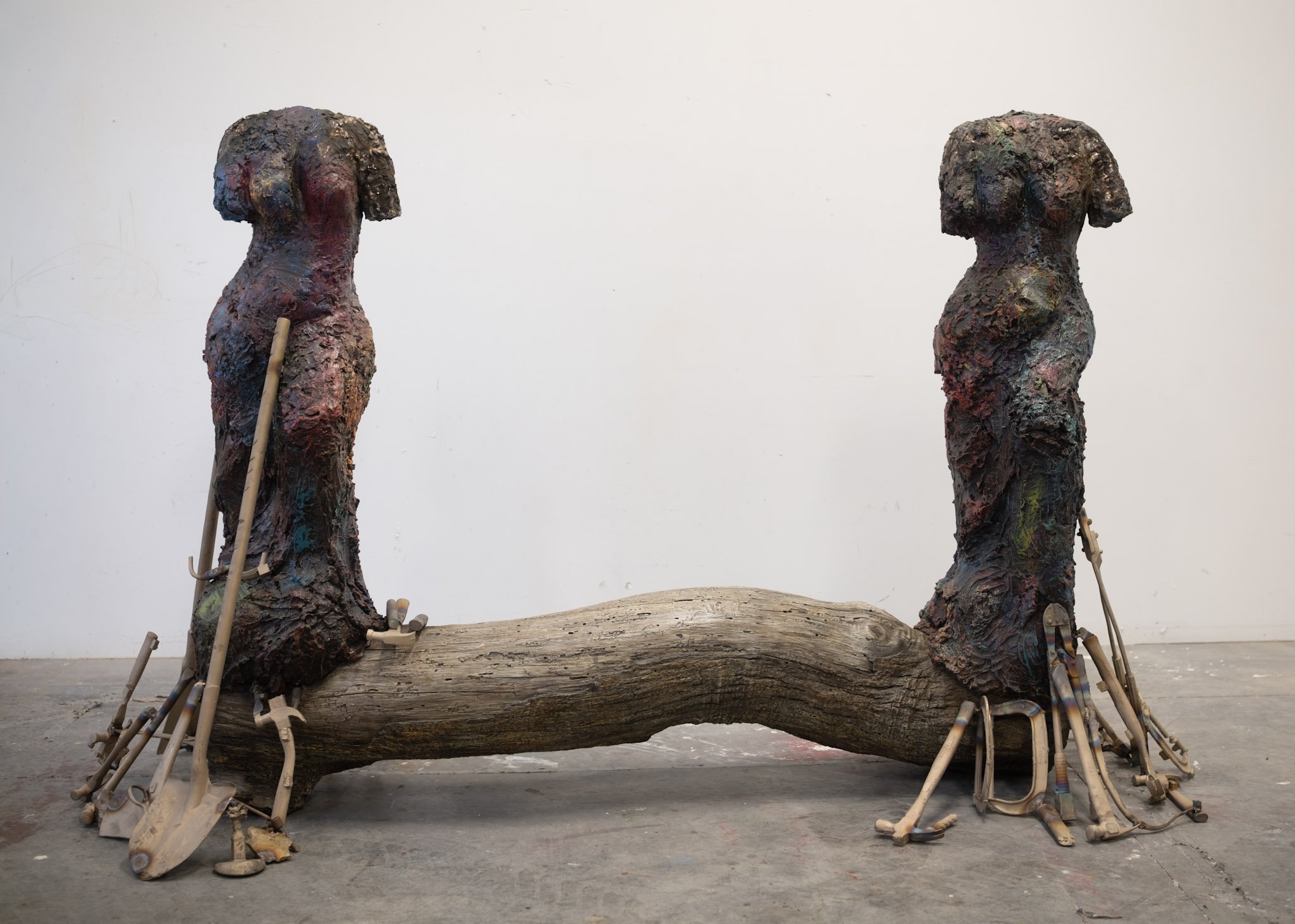 Sculpture with two woman Venus figures on top of a log. Tools beneath them