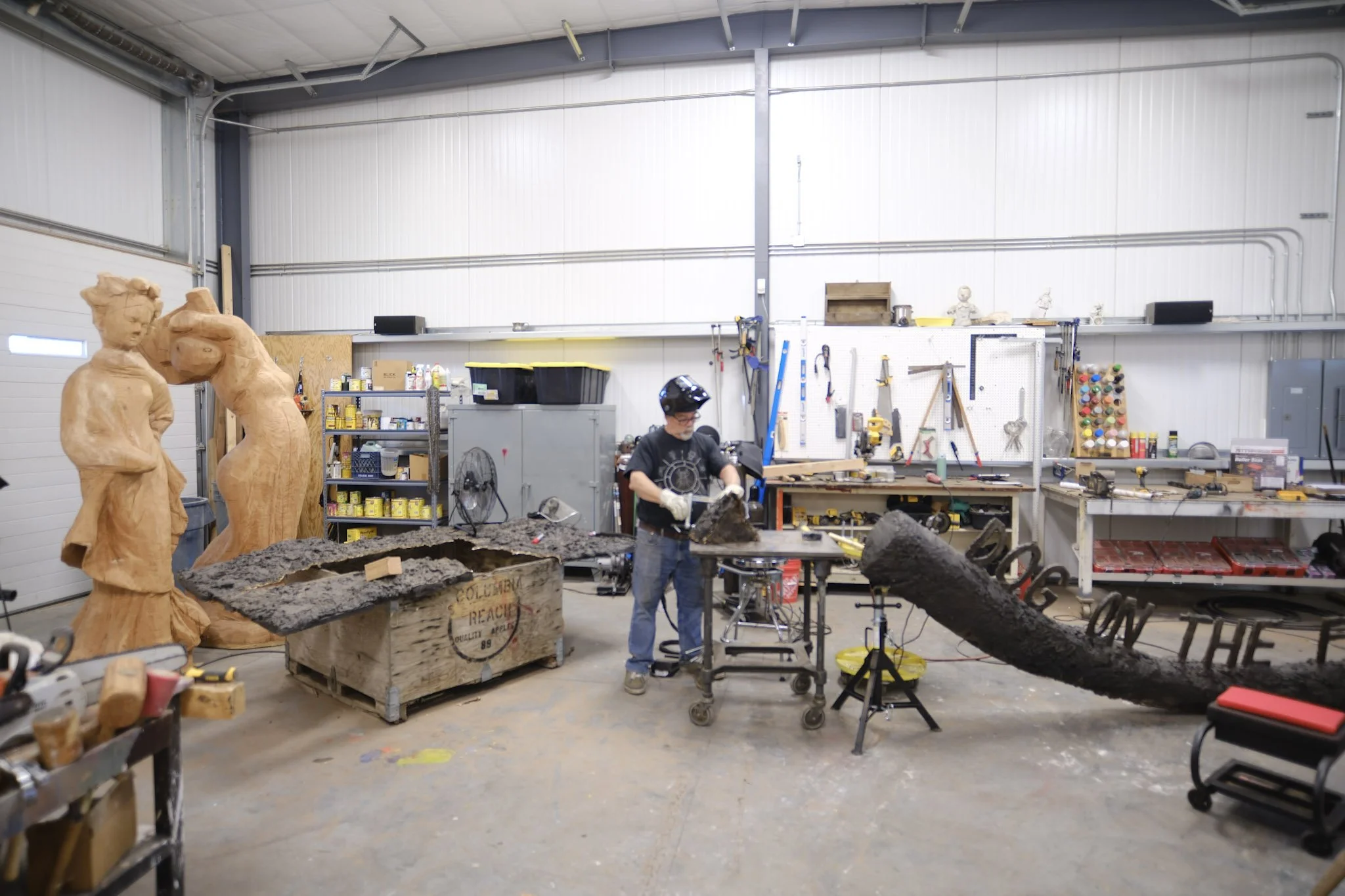 Jim Dines assistant working inside the sudio space with carved wooden sculptures beside him.