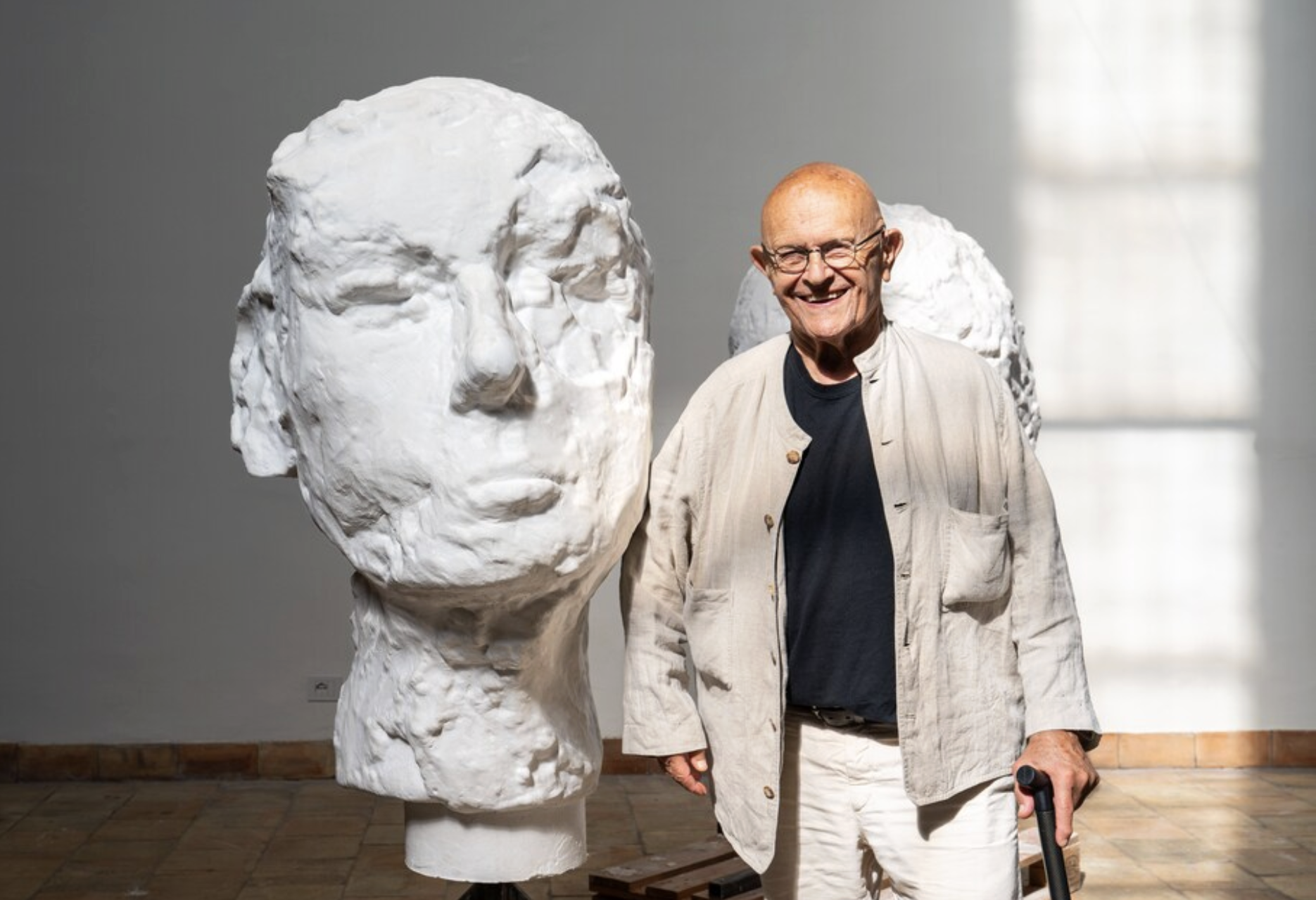 Artist Jim Dine posing alongside a large, white sculpture of a face for the artist's "Elysian Fields" exhibition
