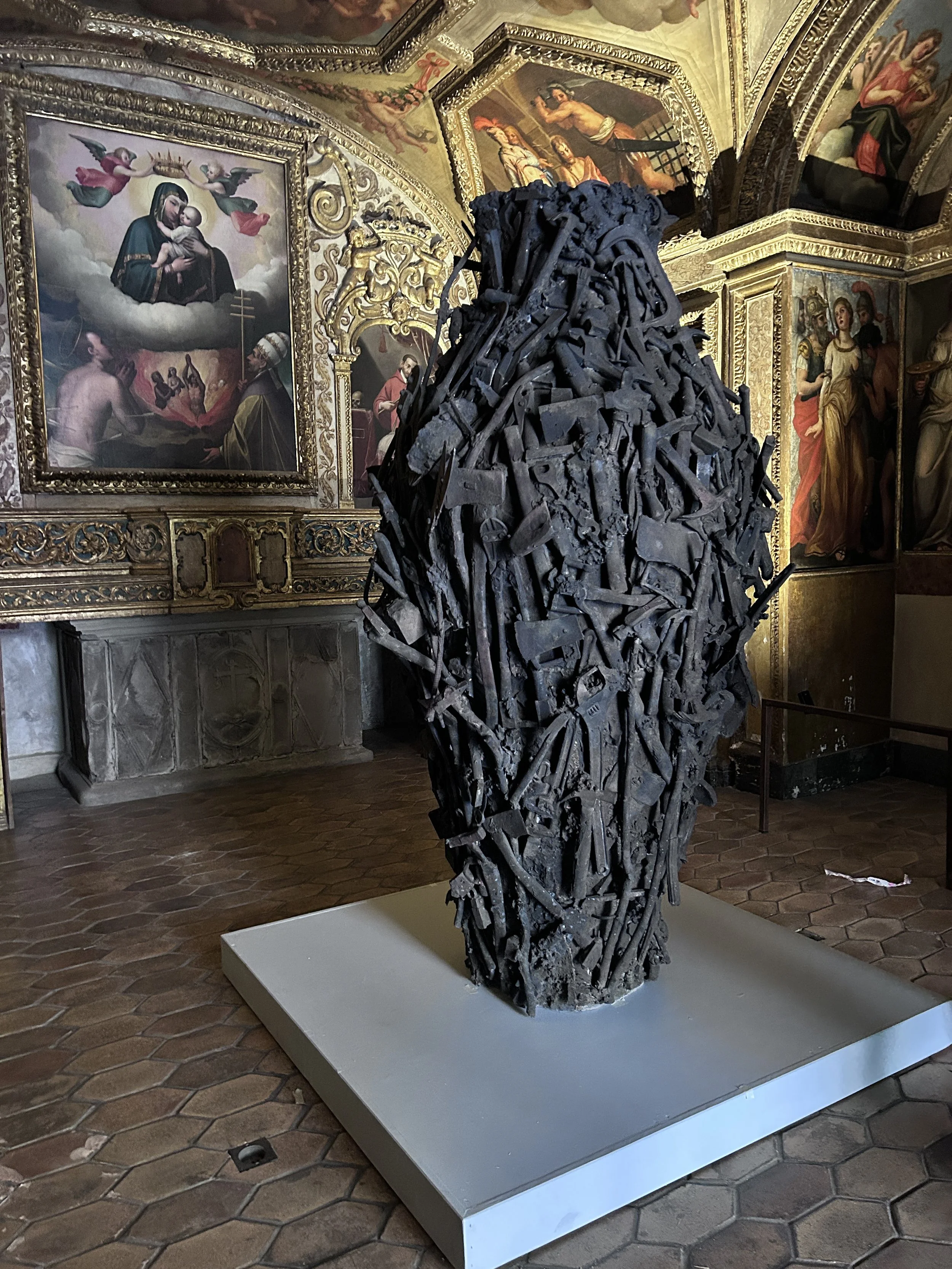 Metal sculpture made from scrap tools in the form of a vessel in front of a religious alter with mother and child