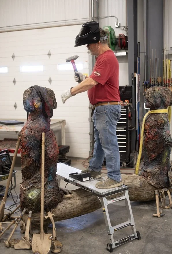 Man welding and hammering a female figure statue
