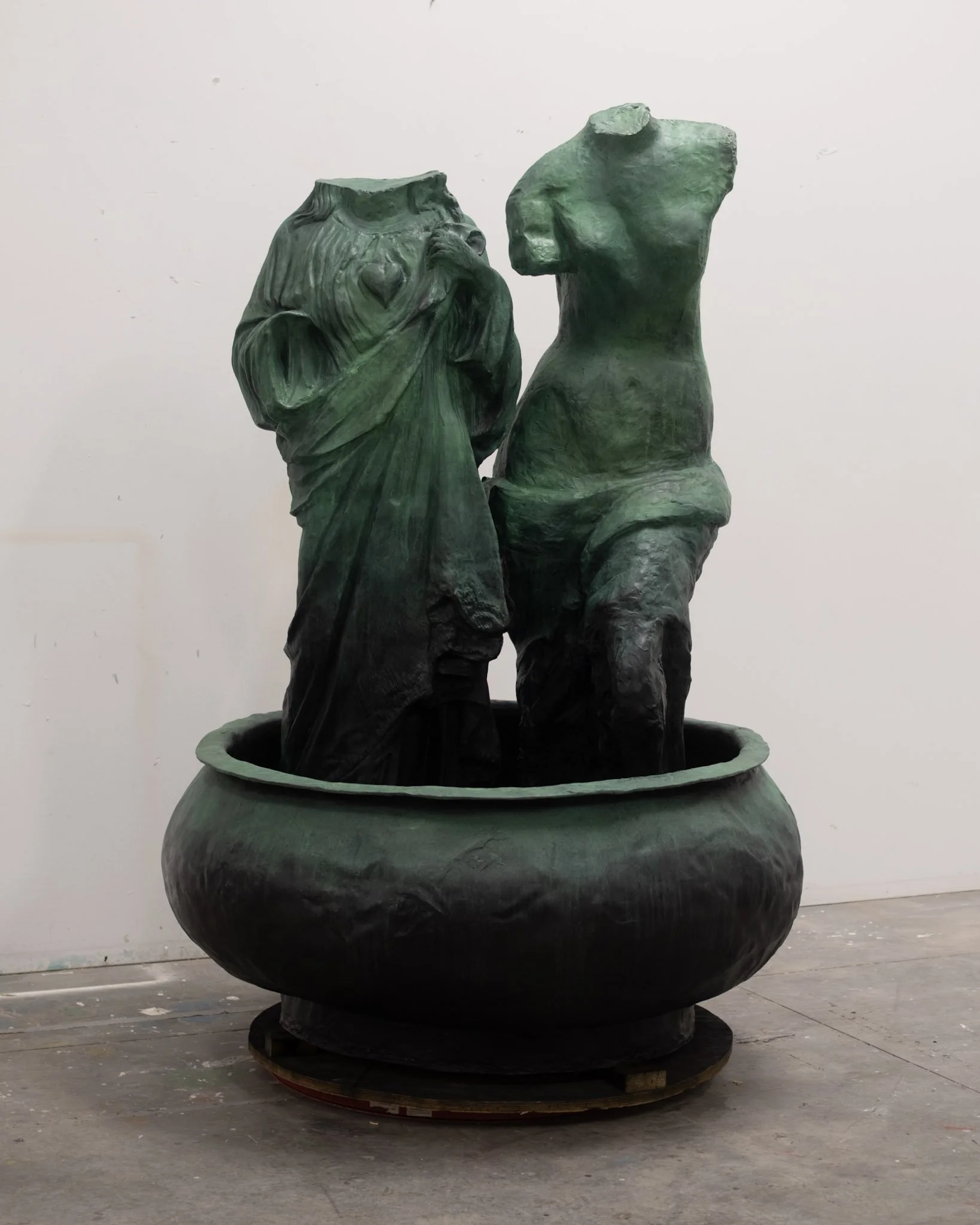 Greek female figure stature next to a mother mary statue both without heads standing inside a bowl