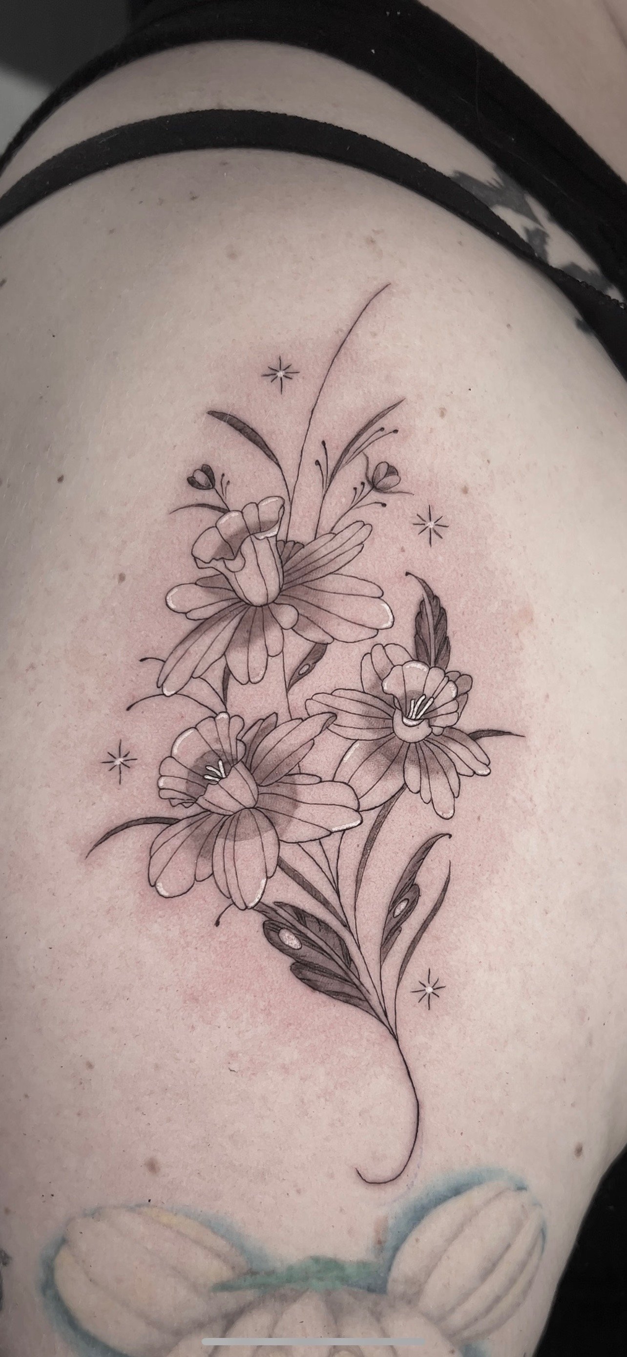 Black and gray floral tattoo of three flowers with detailed petals and leaves on a person's skin by Mando at Harp and Rose Tattoo in Ventura California