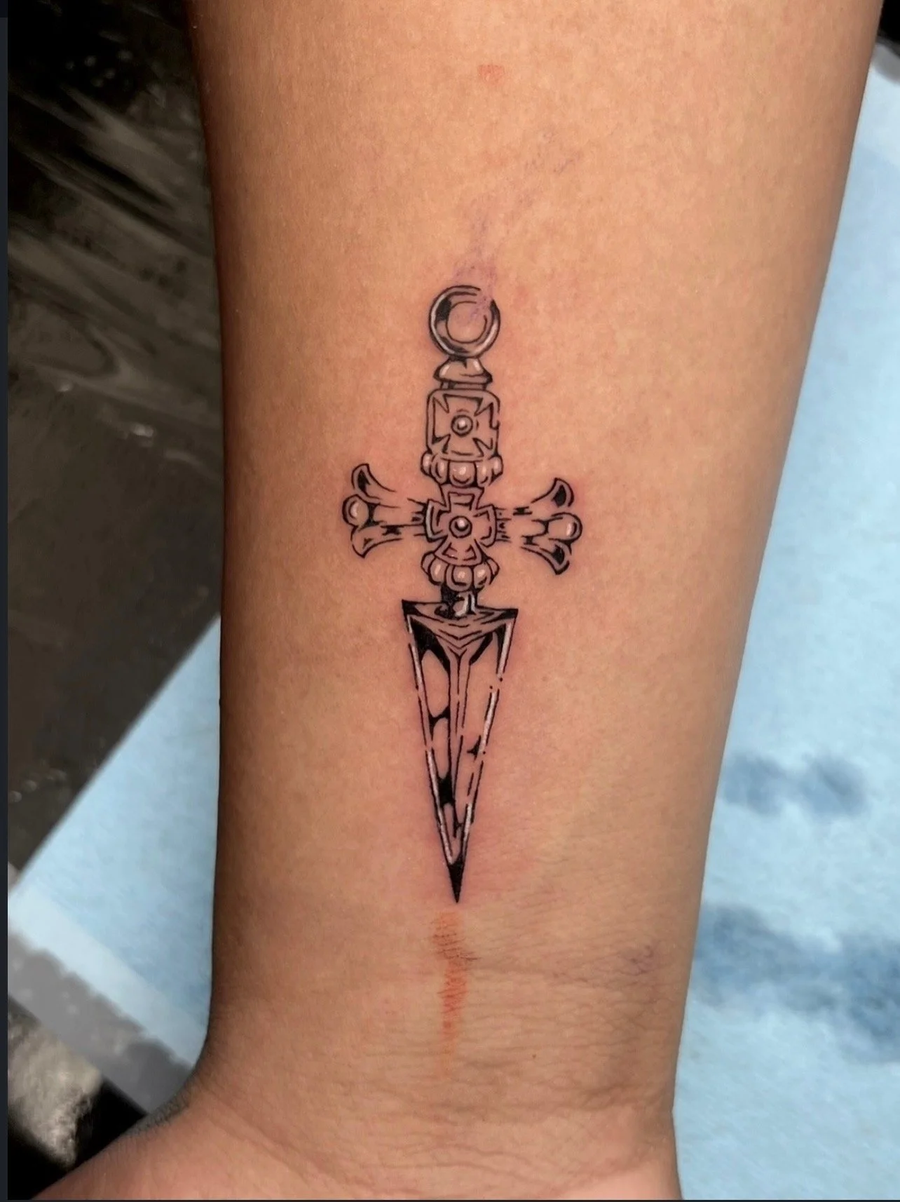 Tattoo of a stylized dagger with ornate details, positioned vertically on a person's lower leg by Mando at Harp and Rose Tattoo in Ventura California