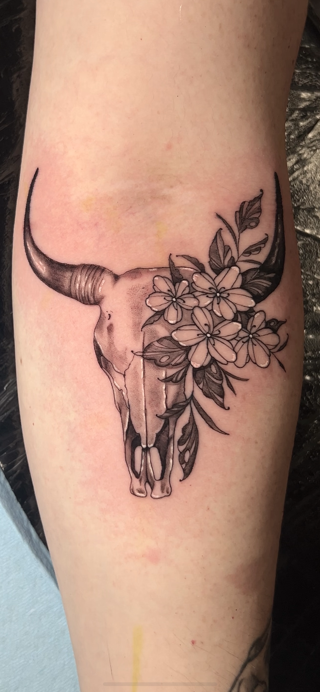 Tattoo of a cow skull with flowers and leaves by Mando at Harp and Rose Tattoo in Ventura California