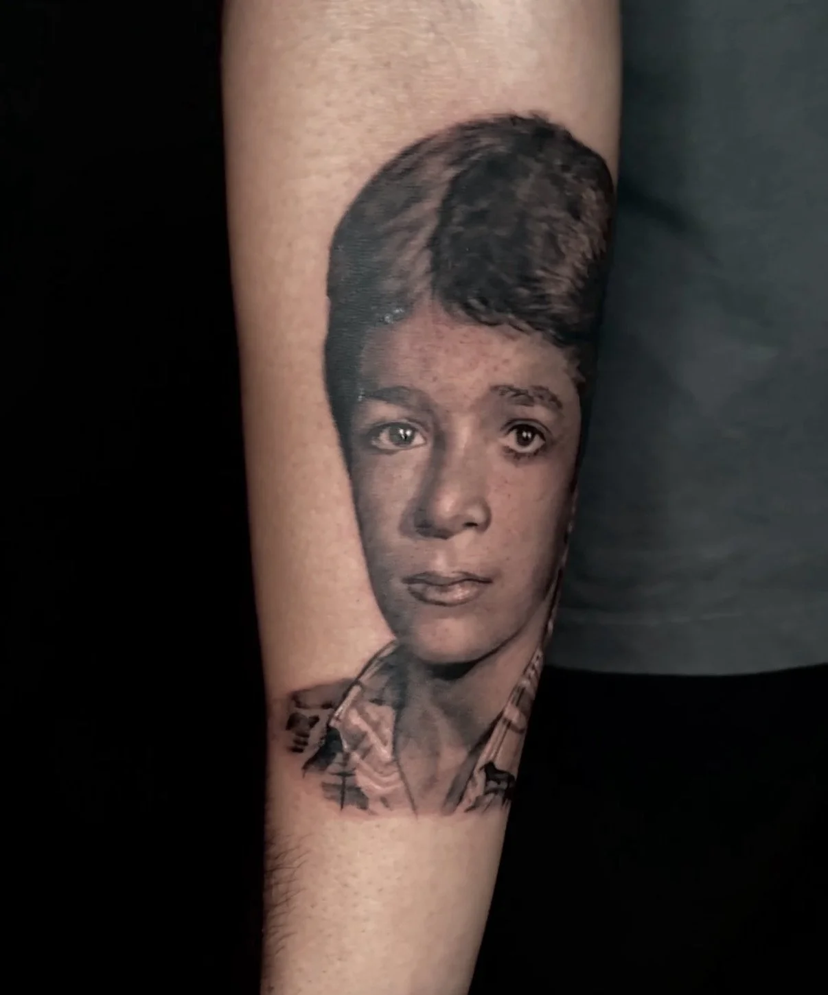 Tattoo of a young boy's face on a person's arm by Harp and Rose Artist Richy Reynolds in Ventura California