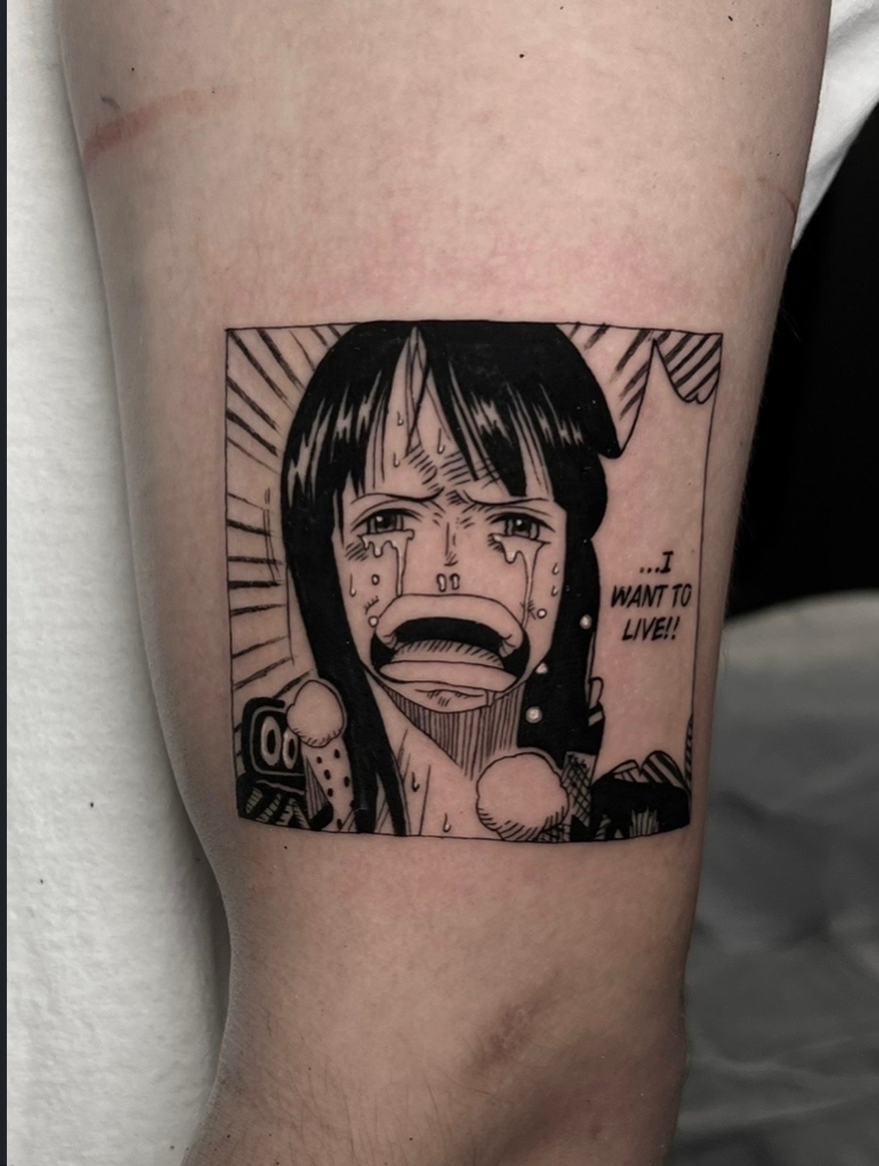 Black and white tattoo of a crying anime girl from One Piece with tears streaming down her face, with the text "...I WANT TO LIVE!!" beside her by Mando at Harp and Rose Tattoo in Ventura California