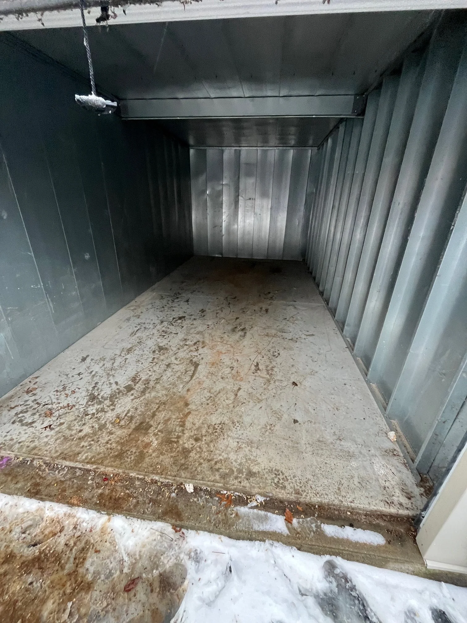 Empty, metallic storage shed with a concrete floor, standing on snow outside.