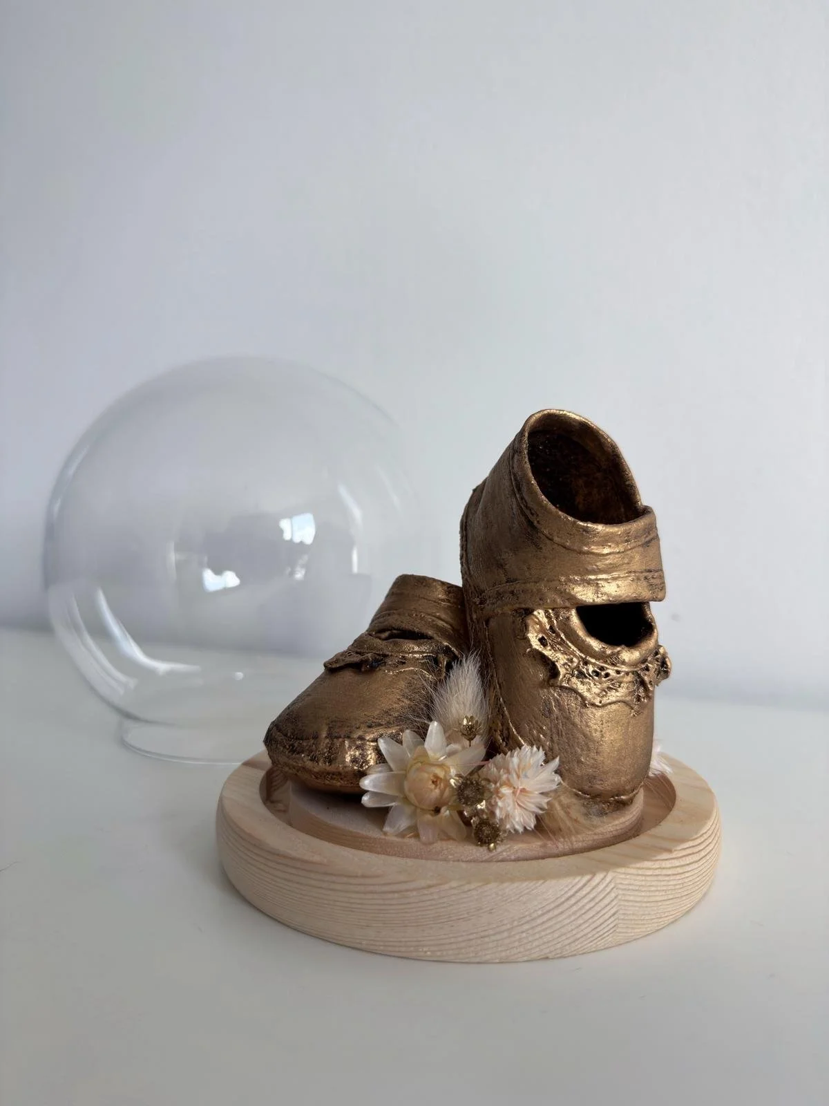 Verbronzing van babyschoentjes in kleine bolvormige stolp met droogbloemen