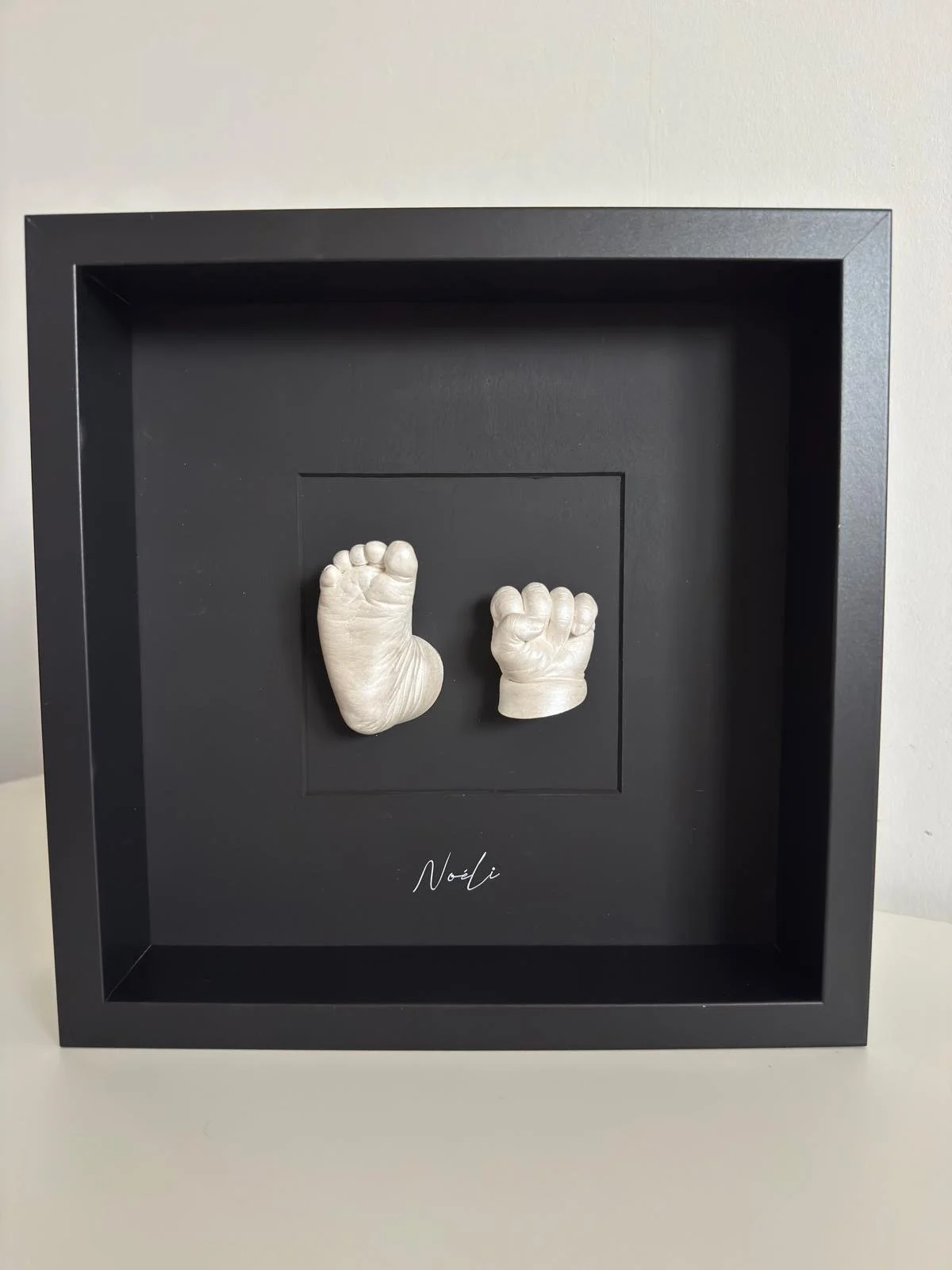volledig zwarte kader en zwarte achtergrond kader met afdruk van baby hand en voet in de kleur parelmoer