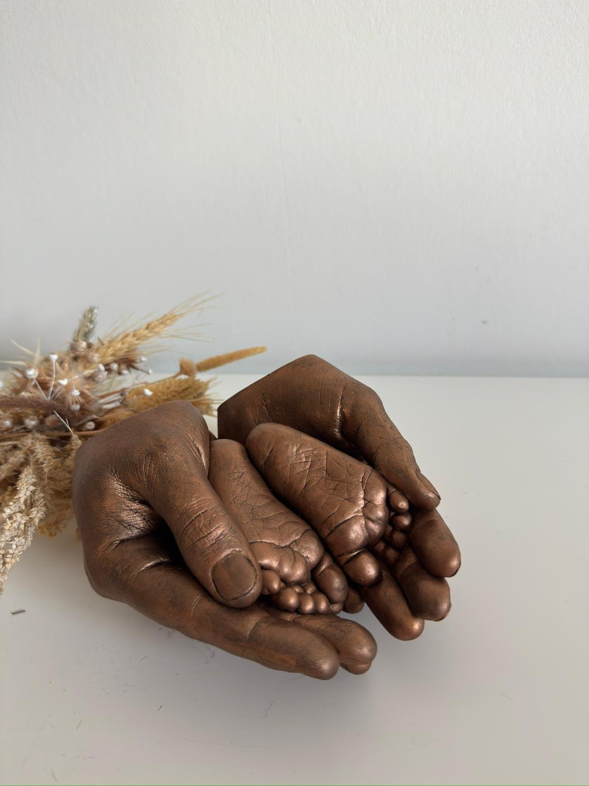 Afdrukje van 2 babyvoetjes in de afdruk van de handen van de ouders in kleur brons