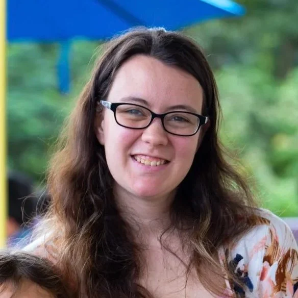 Mountain landscape with a lake in front, grassy hills, and a cloudy sky.