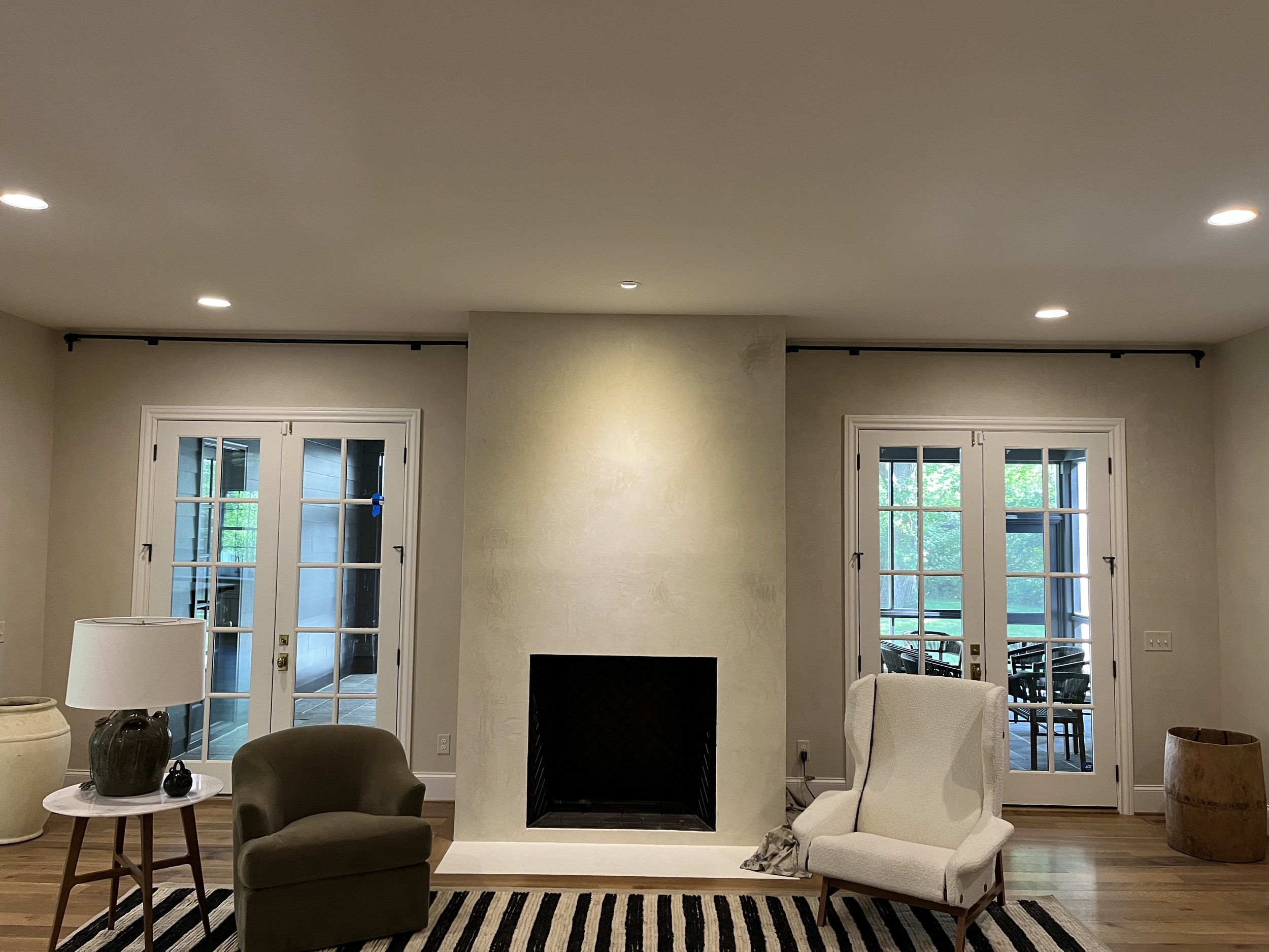 Living room with fireplace, two armchairs, striped rug, and French doors