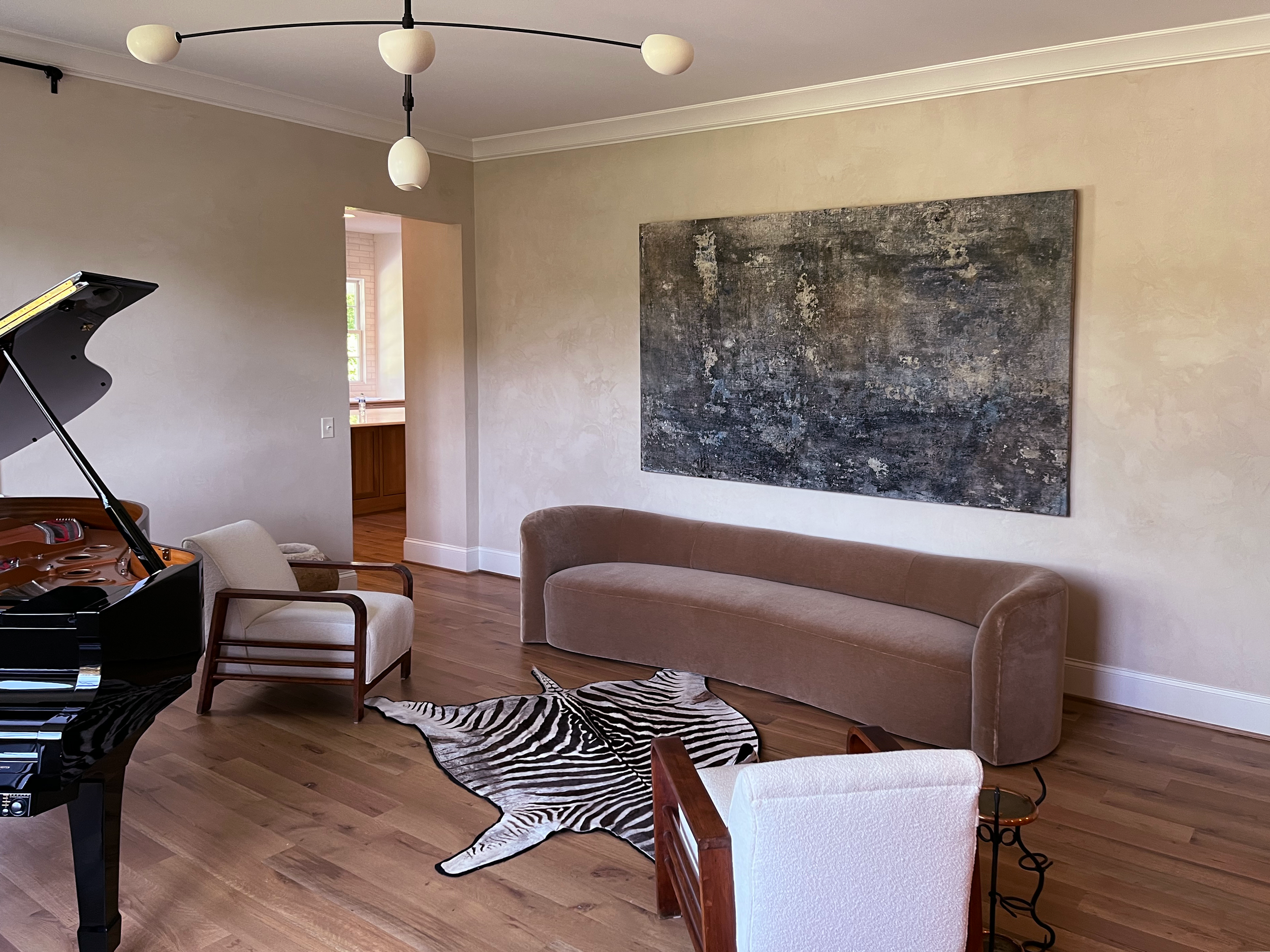 Modern living room with grand piano, beige sofa, abstract wall art, zebra print rug, and white armchair.
