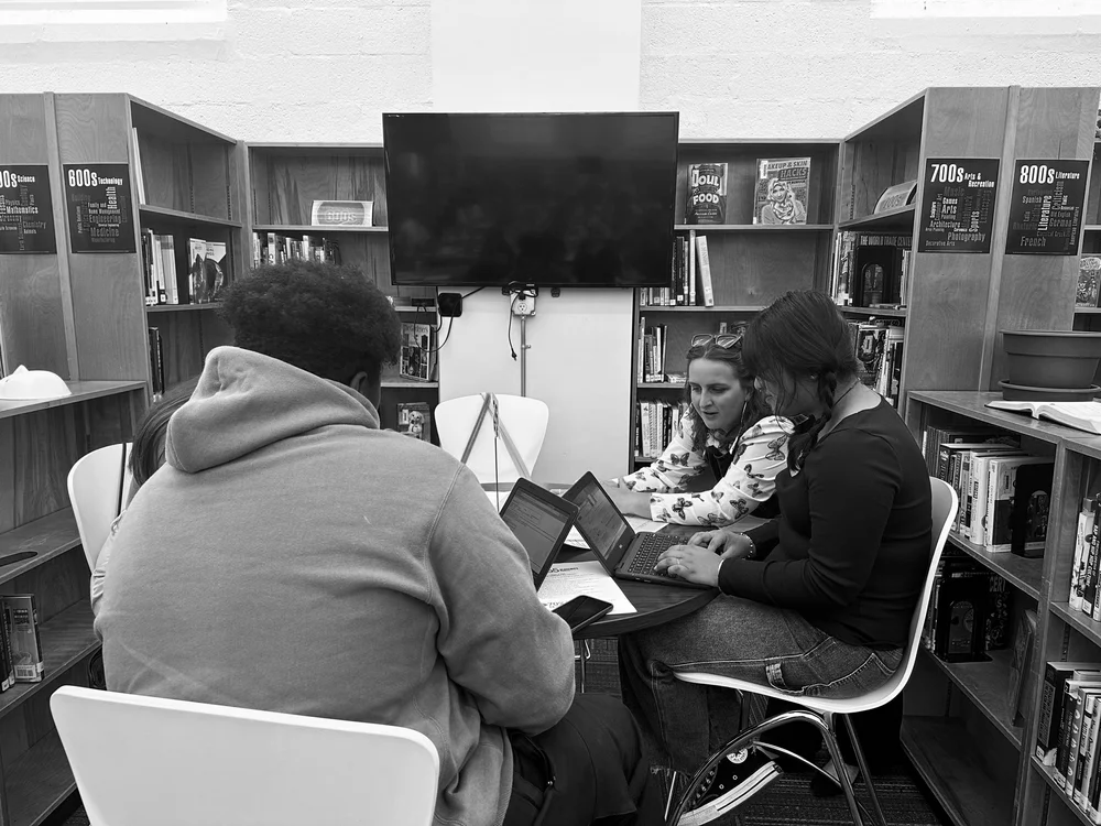 High school students work on laptops at a table in a school library