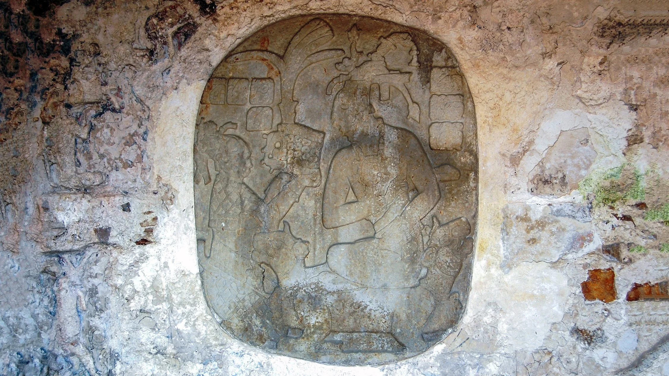 an oval relief sculpture shows a woman handing a feathered crown to a man on a throne