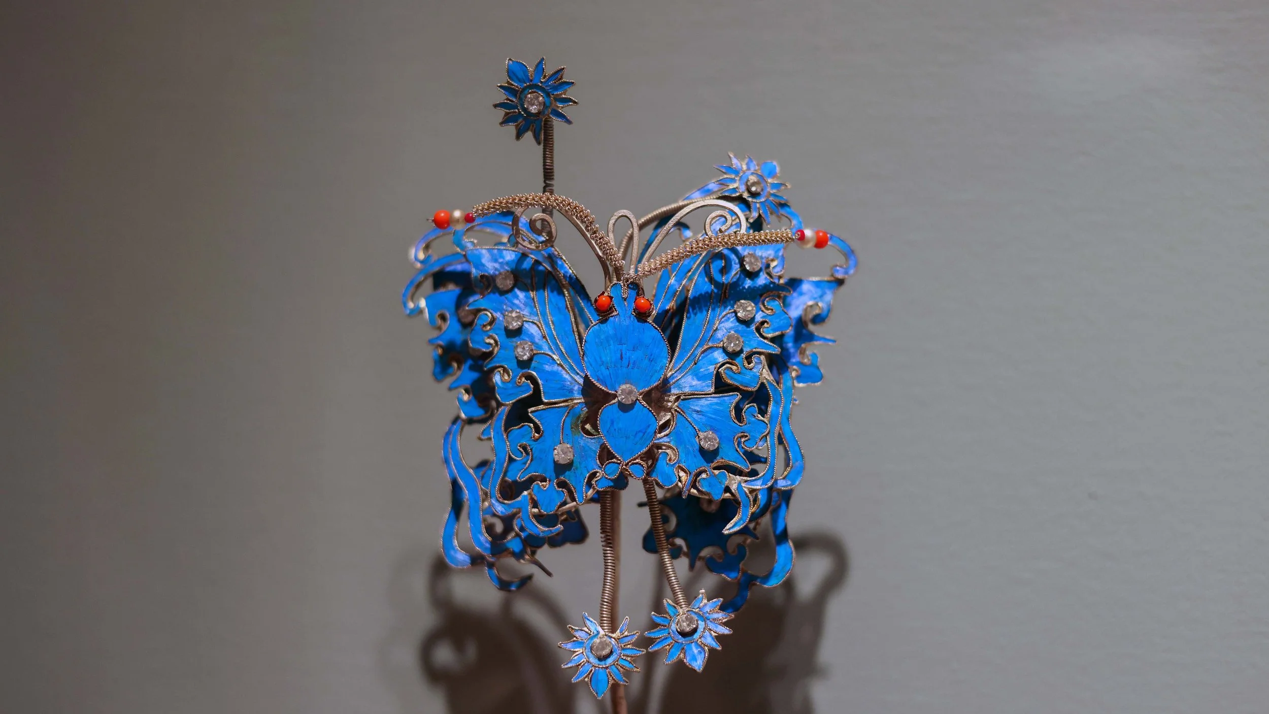 A decorative butterfly-shaped jewelry piece with blue and silver colors, accented with small red and clear stones.