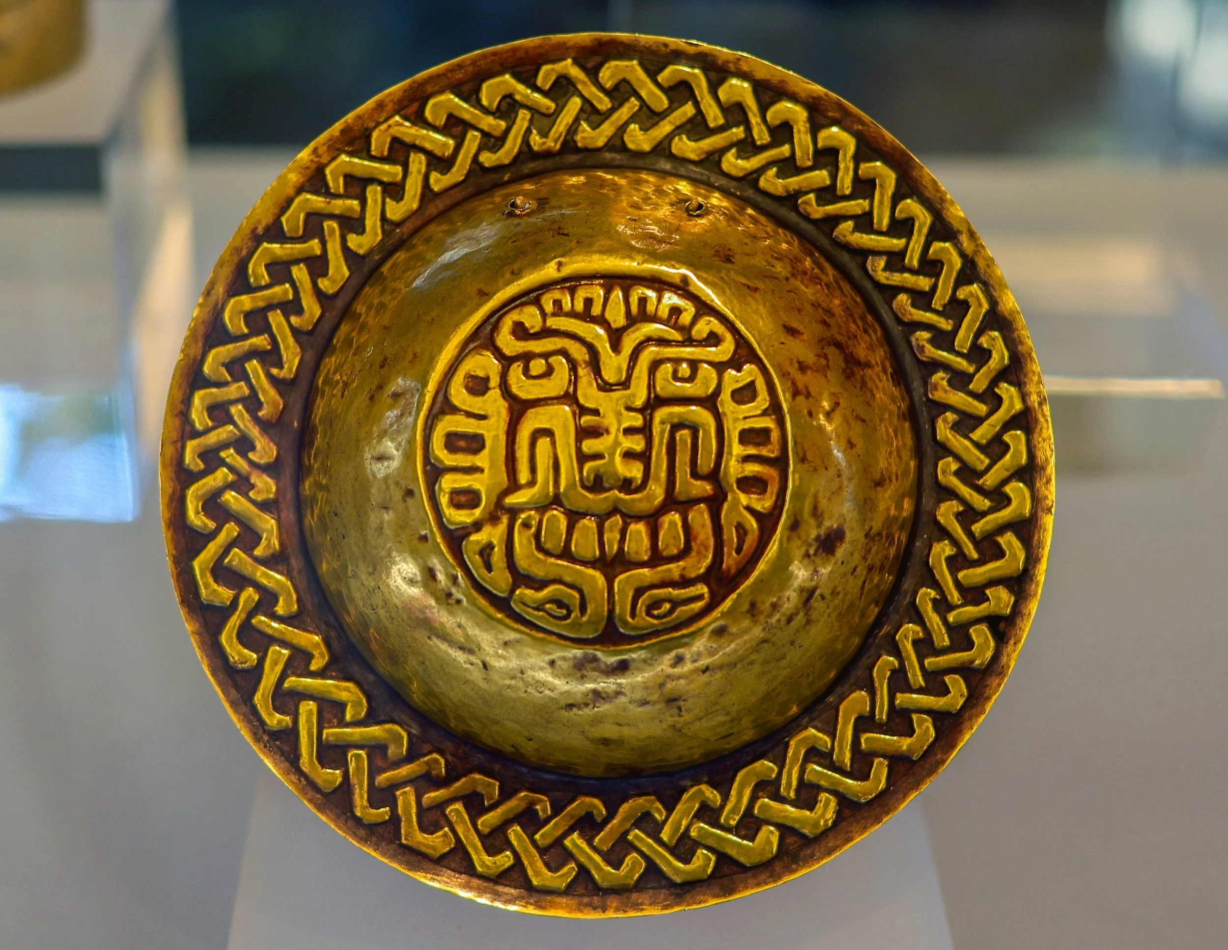Close-up view of golden andean decorative object with geometric patterns and designs.