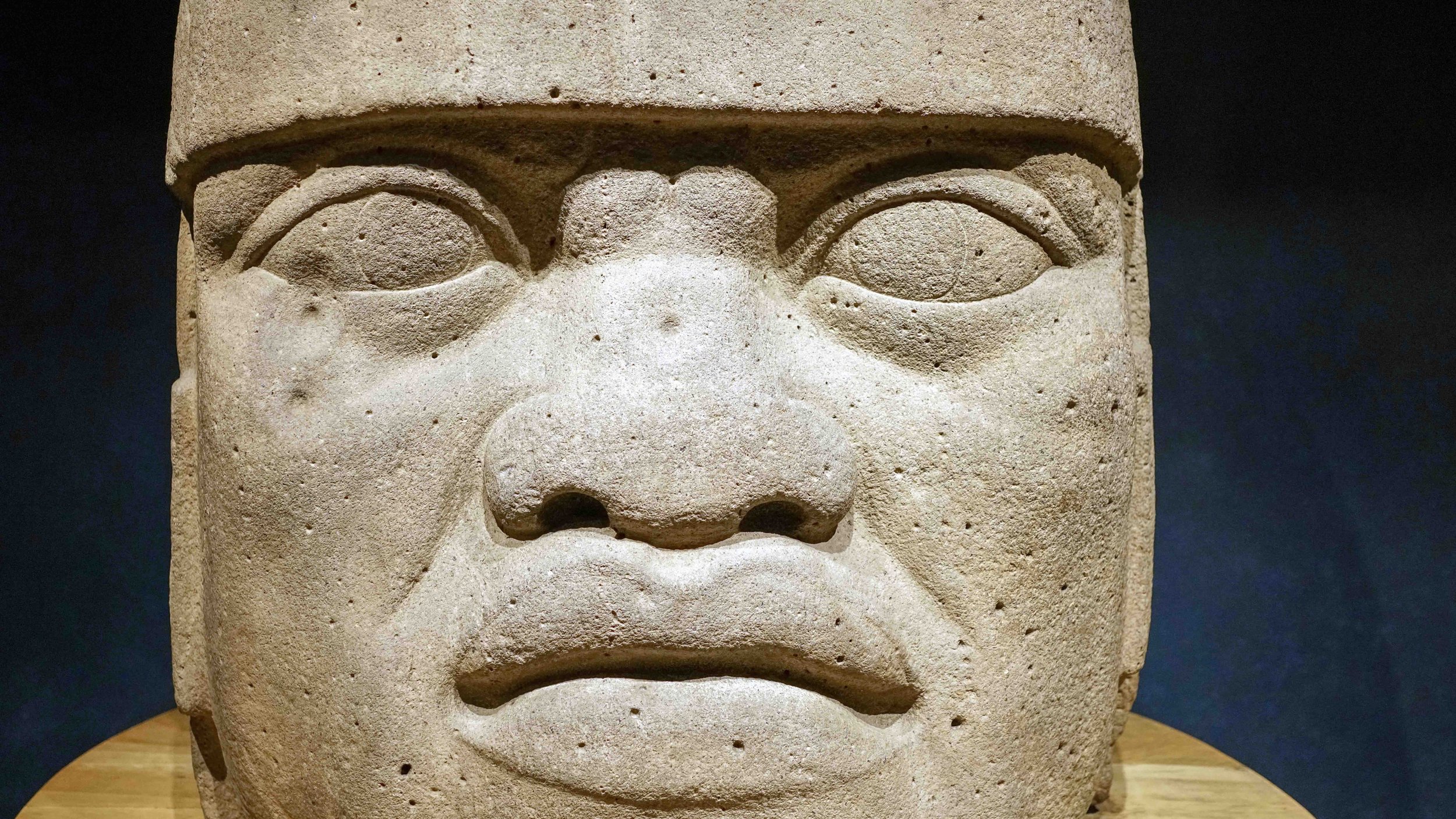 Close-up of an ancient stone carving of a human face with detailed eyes, nose, and mouth, set against a dark background.