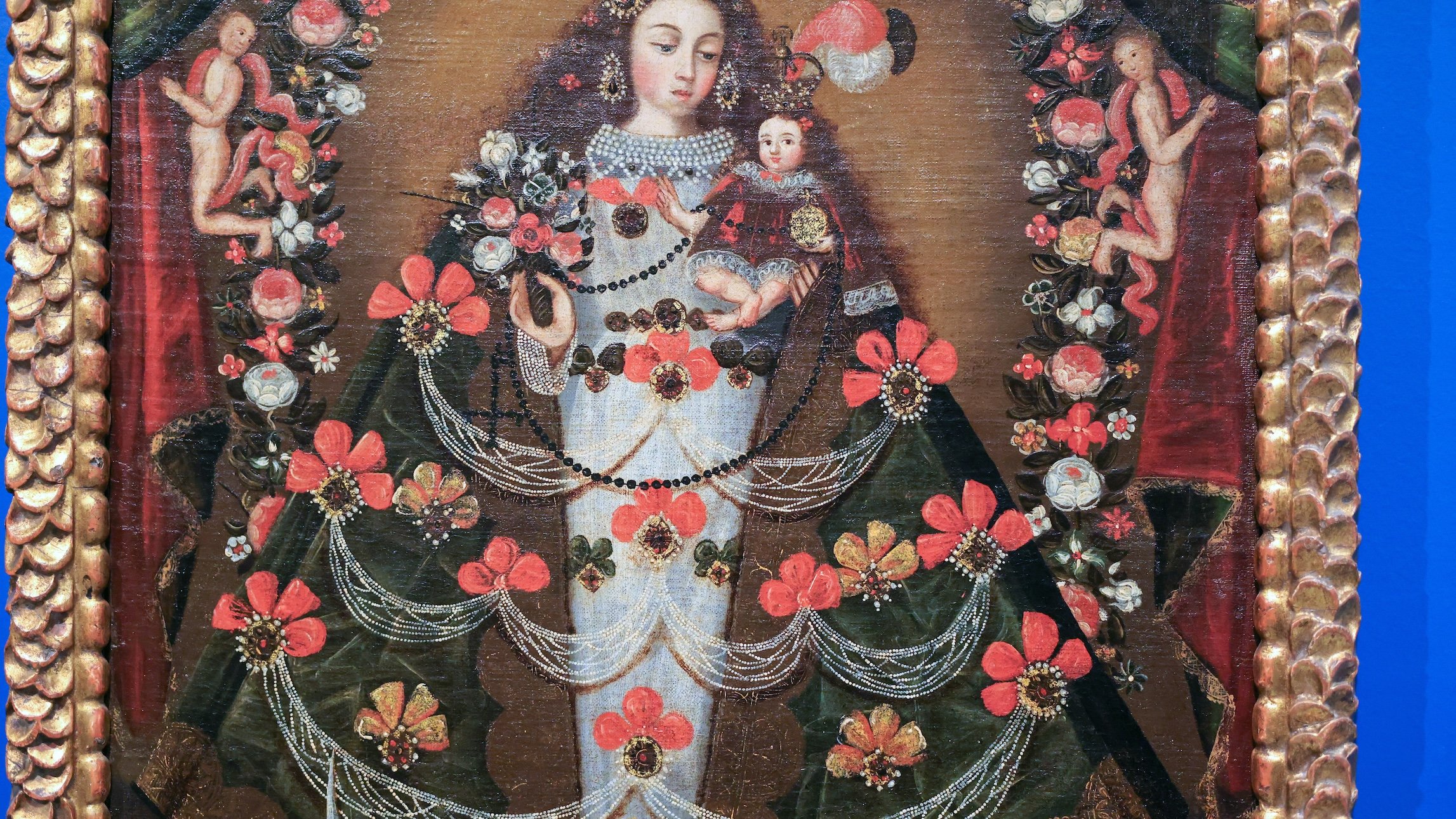 Traditional painting of the Virgin Mary holding baby Jesus, surrounded by flowers and intricate jewelry, with a decorative golden frame.