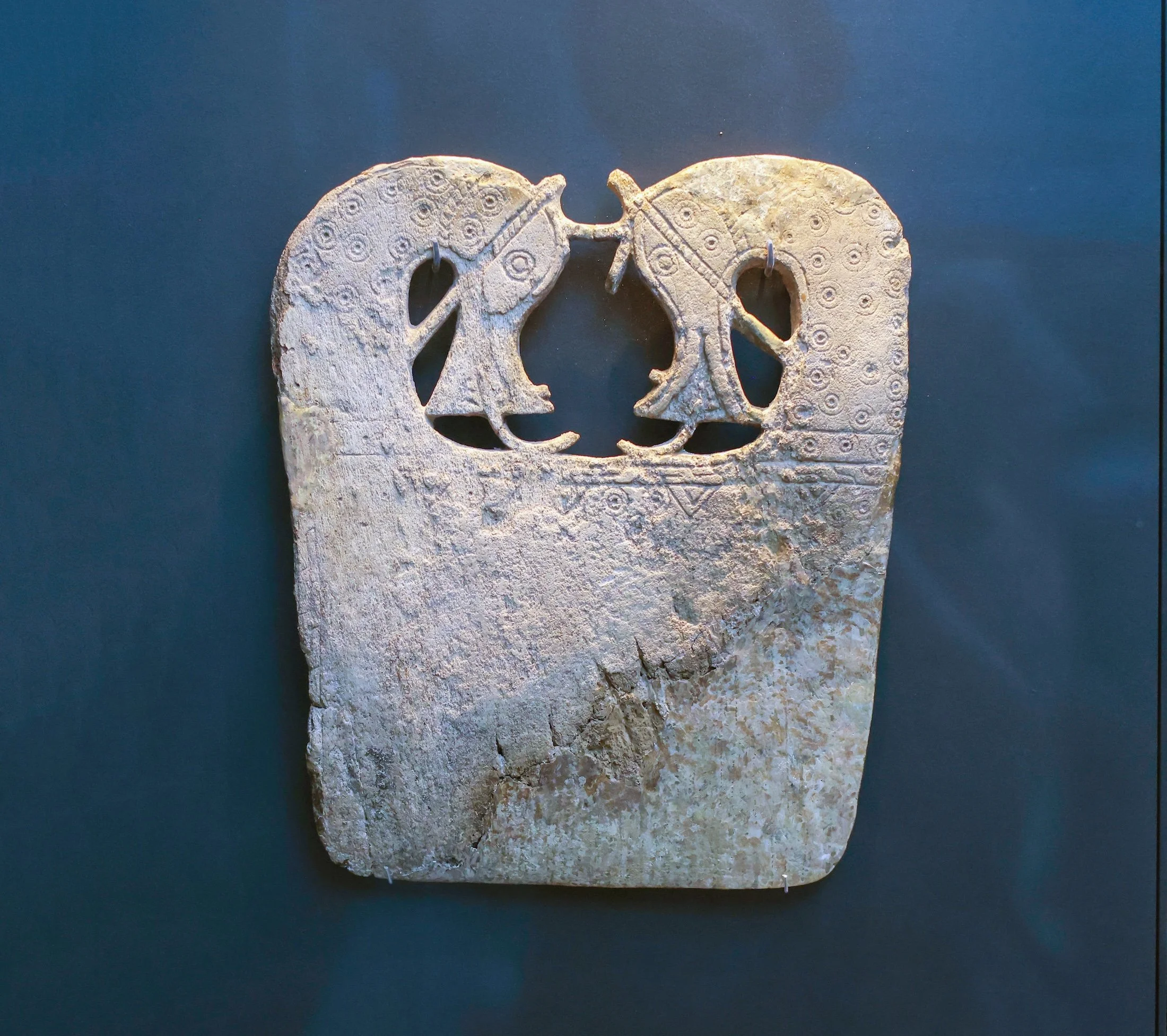 Ancient carved stone depicting two abstract bird figures facing each other against a dark background.