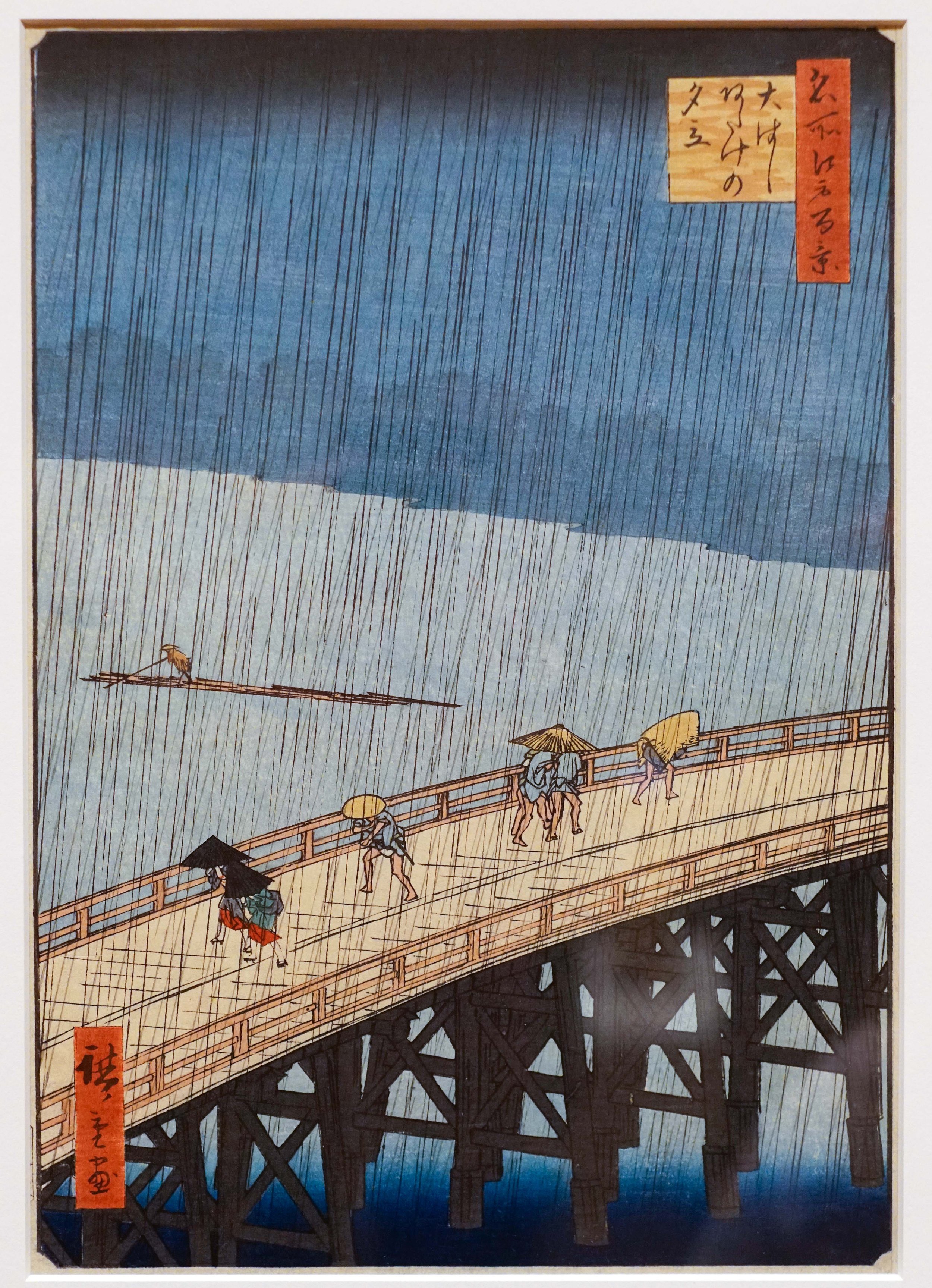 Traditional Japanese woodblock print depicting people walking on a bridge during rain, with umbrellas and a large body of water below.