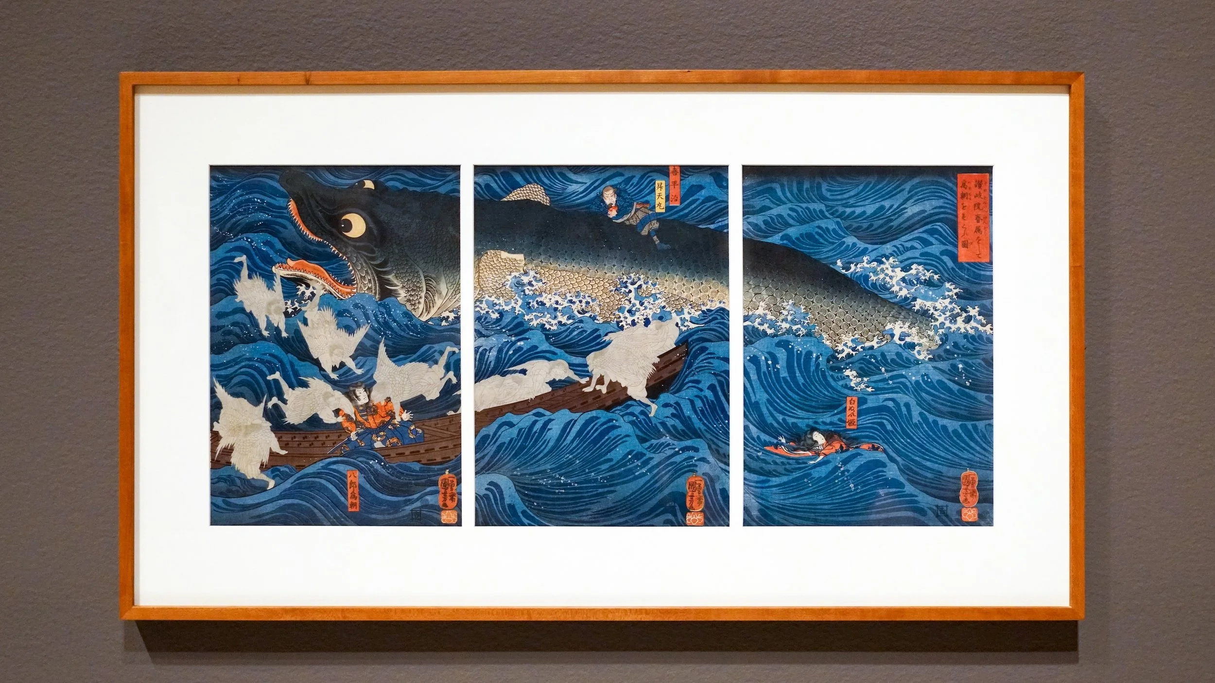 Triptych of traditional Japanese woodblock print depicting a large sea monster attacking a boat, with waves and fishermen.