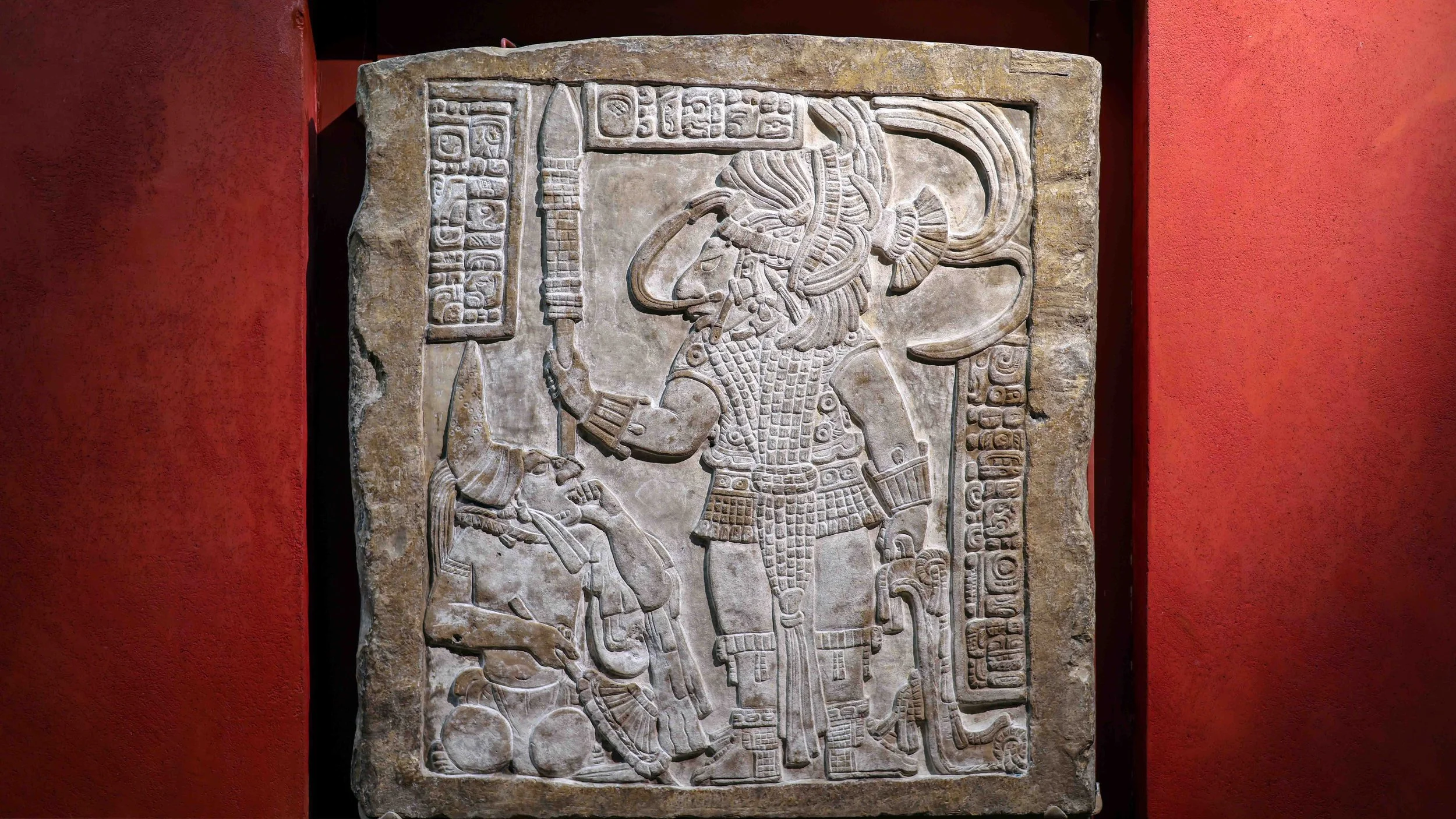 Ancient stone carvings of Mayan figures and symbols on a wall.