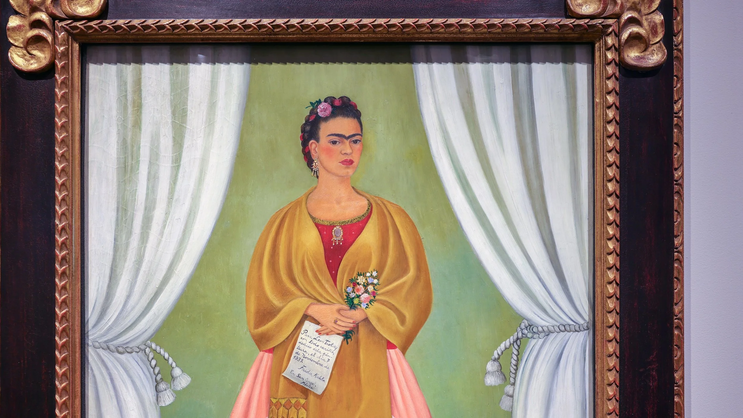 Portrait of Frida Kahlo, She wears a golden shawl and holds a boquet of pastel flowers in her hands.
